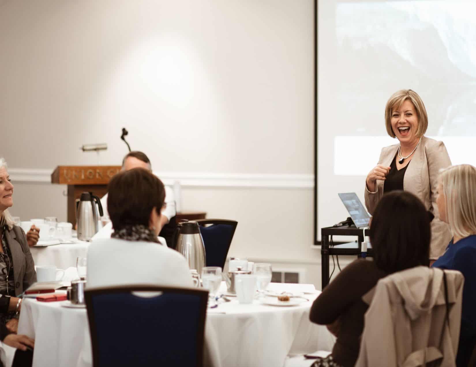 Leader mid-presentation, sharing a light-hearted moment with her audience—modeling joy as a leadership strategy, not a distraction.