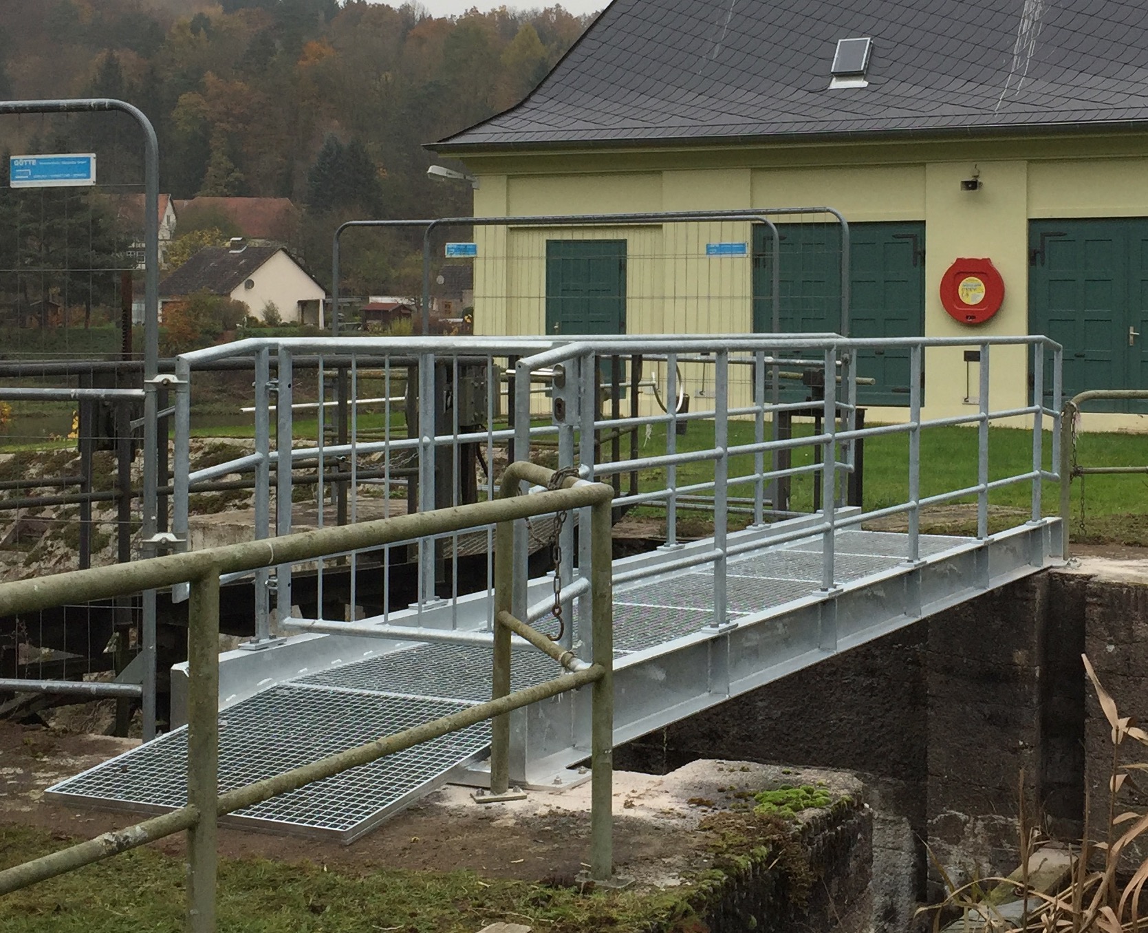 Eine feuerverzinkte Stahlbrücke mit Gitterrost-Lauffläche und stabilen Geländern über eine Betonkonstruktion, gefertigt von Stahlbau von Stahl- und Metallbau Drost.