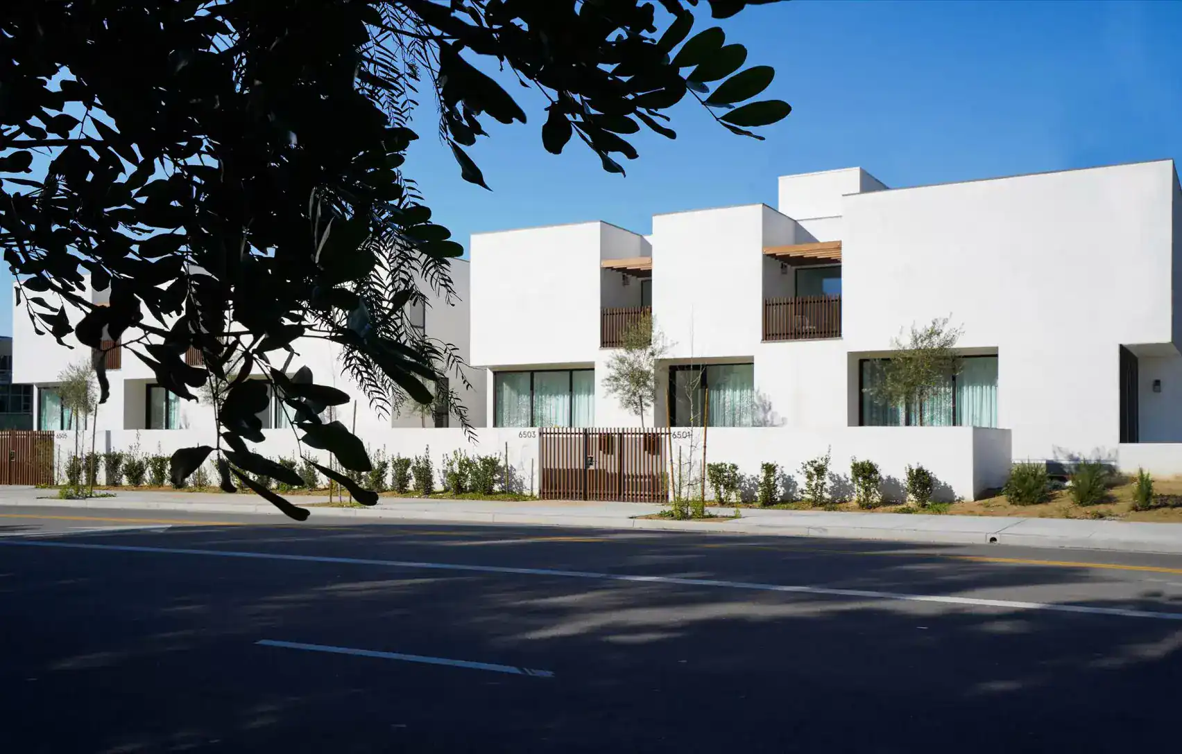 Modern white stucco residential buildings with flat roofs and wooden accents, set against a clear blue sky.