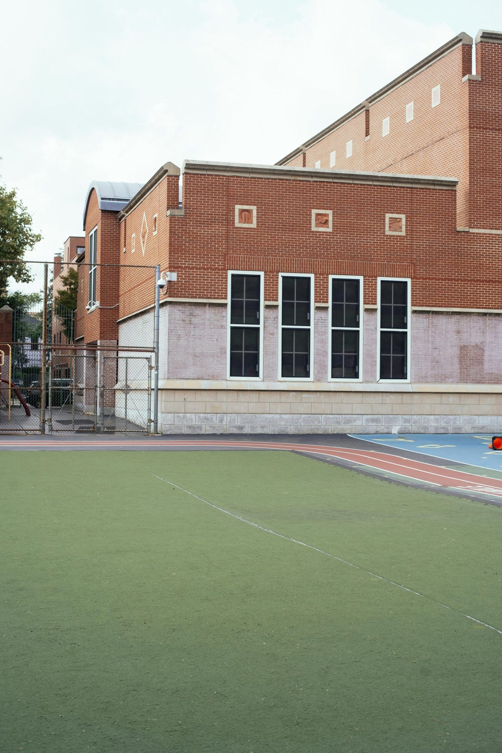 Exterior of red brick building of school with sports ground with synthetic grass