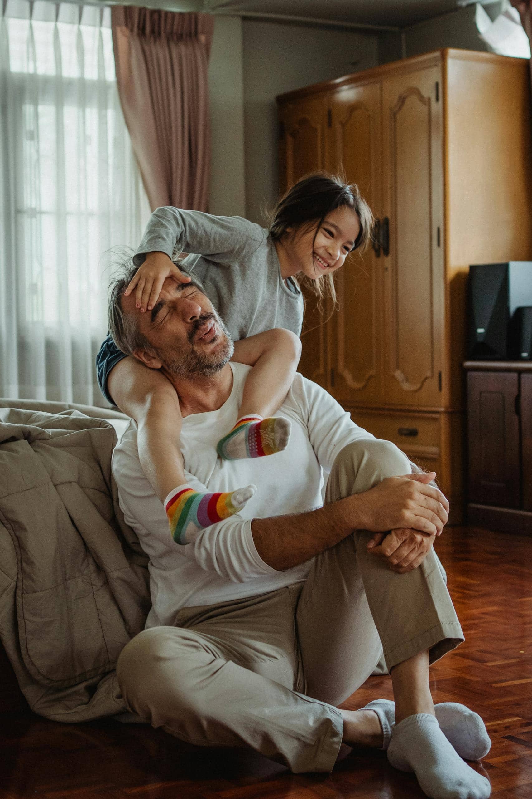 A father and daughter with ADHD enjoy playful bonding time indoors, sharing happiness and laughter addressing ADHD symptoms.