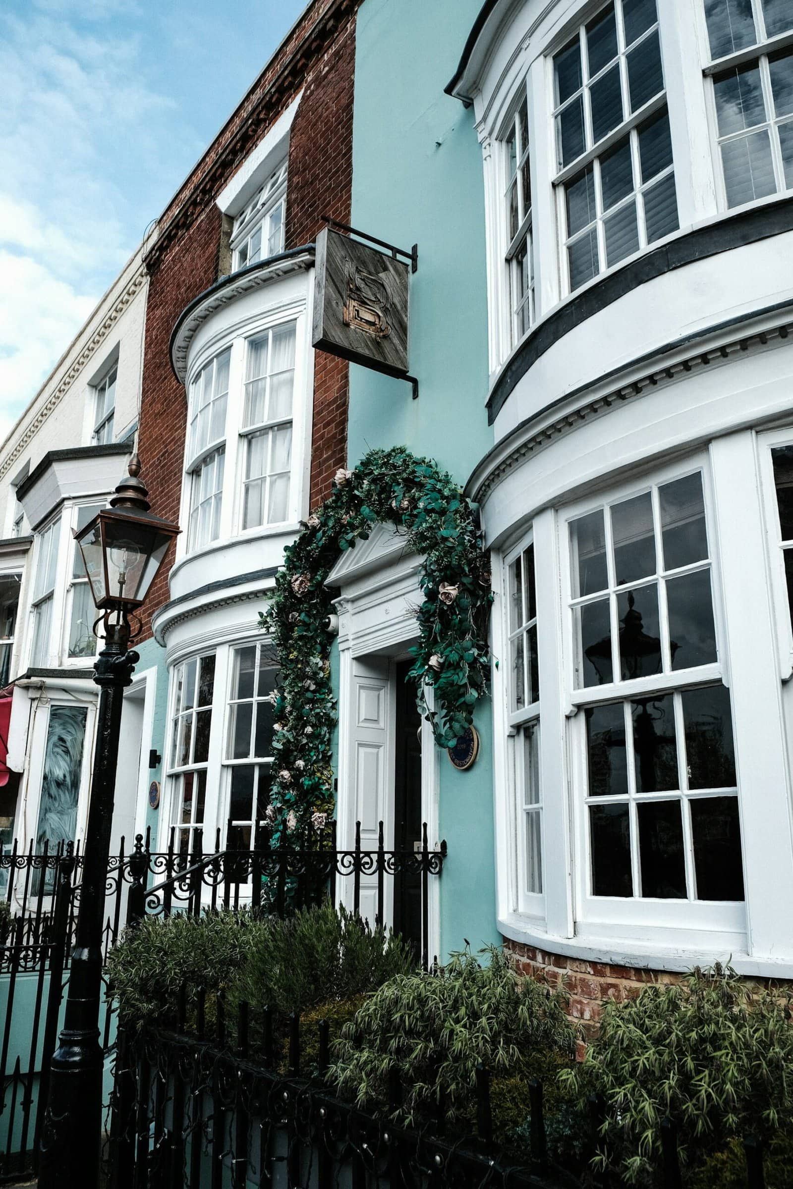 Classic home renovation trends 2026 featuring pastel blue exterior facade, bay windows, and a green entryway arch.