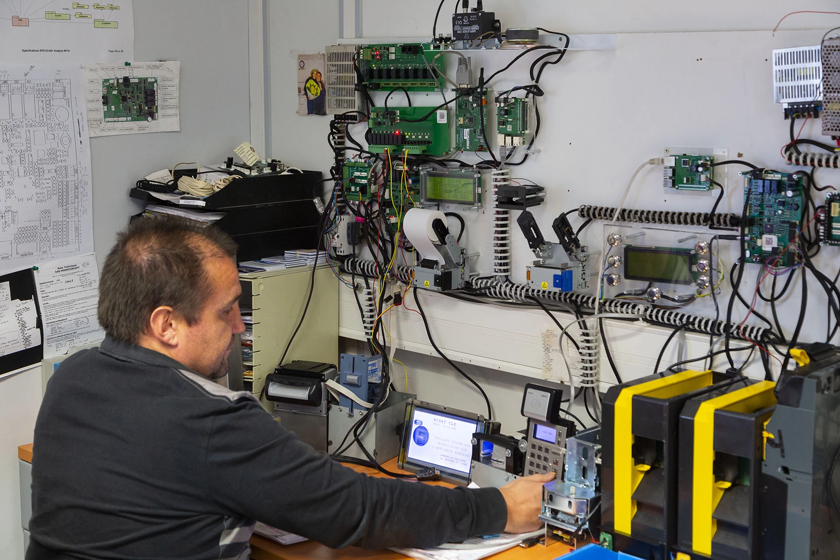 Un technicien travaille dans un laboratoire avec divers équipements électroniques et schémas. Il utilise un ordinateur por