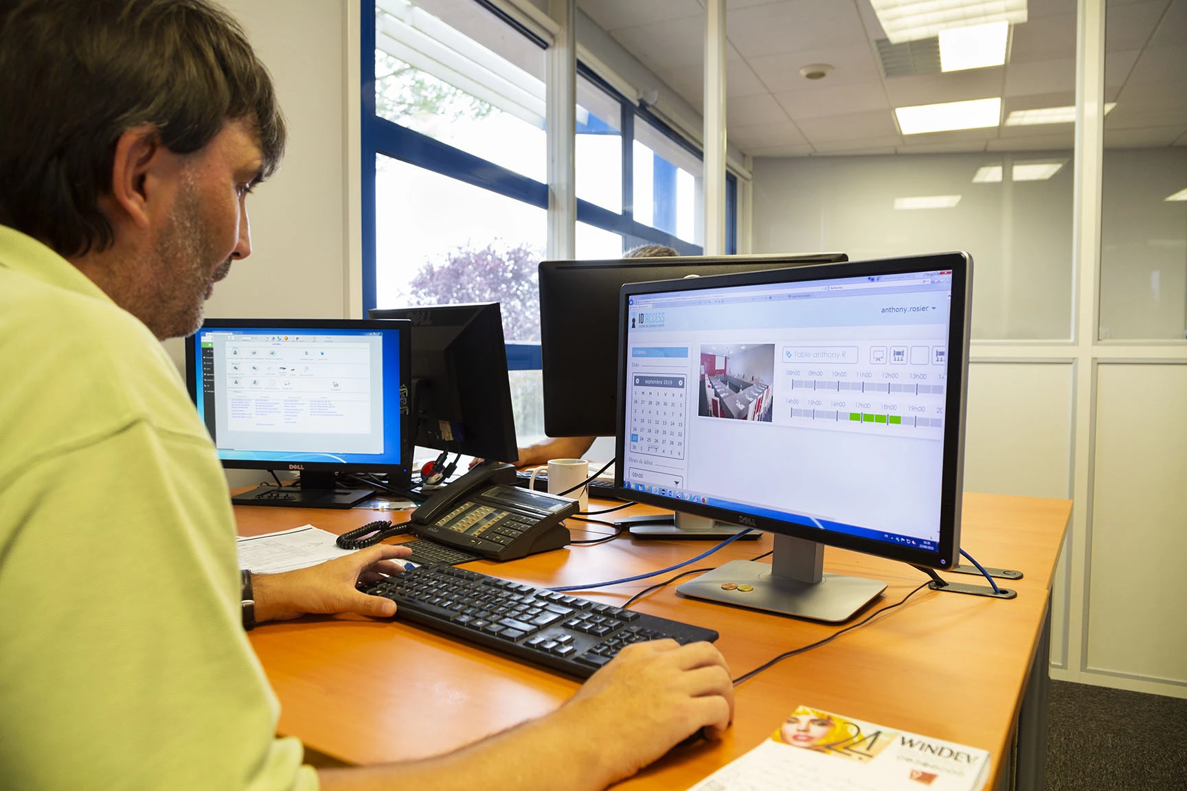 Un homme travaille à un bureau avec deux écrans d'ordinateur dans un espace de travail moderne.