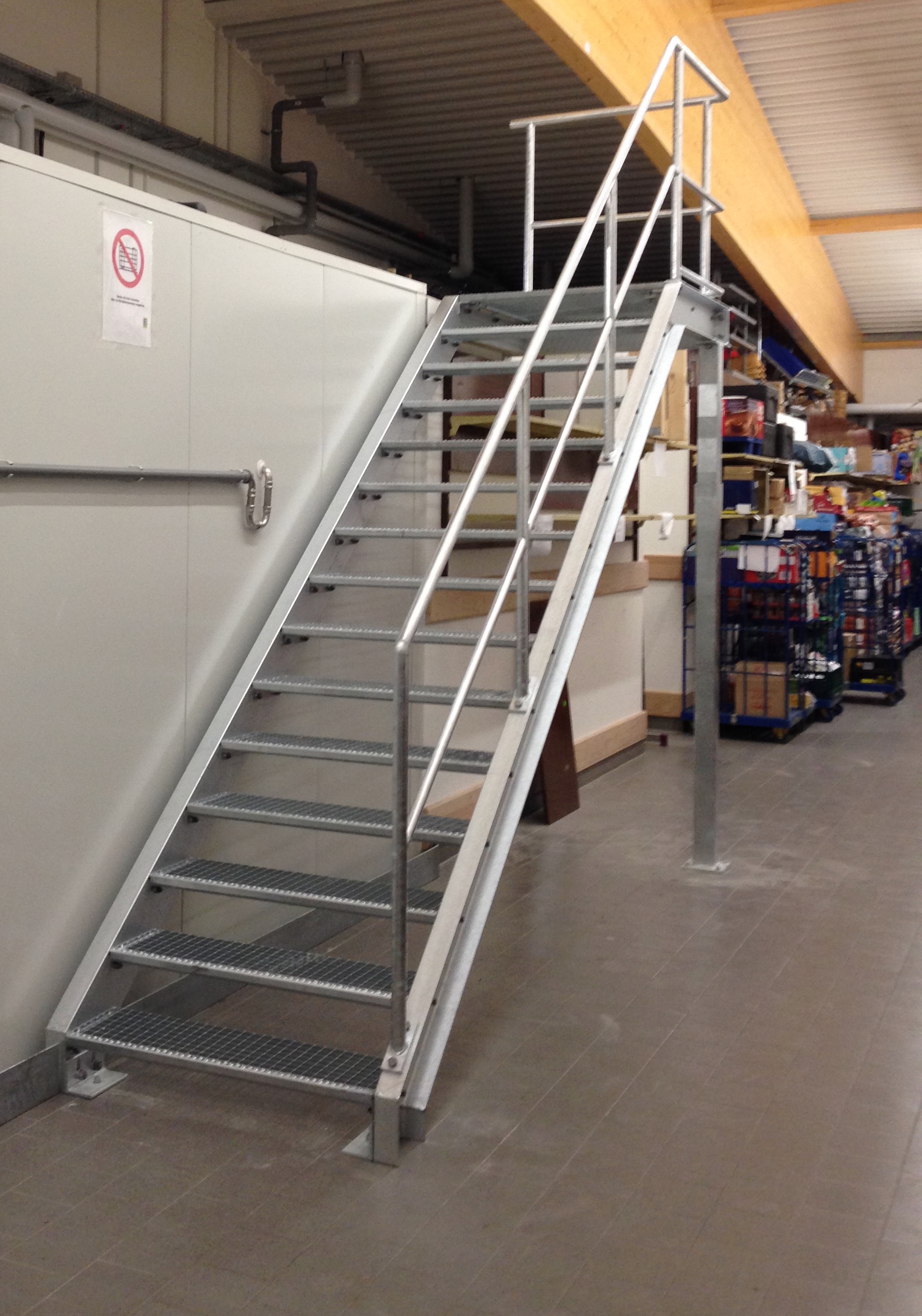 Robuste, feuerverzinkte Metalltreppe mit Gitterroststufen und beidseitigem Geländer von Stahl- und Metallbau Drost in einer Industriehalle.