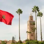 The Moroccan flag waves in front of a clock tower, symbolizing national pride and heritage.