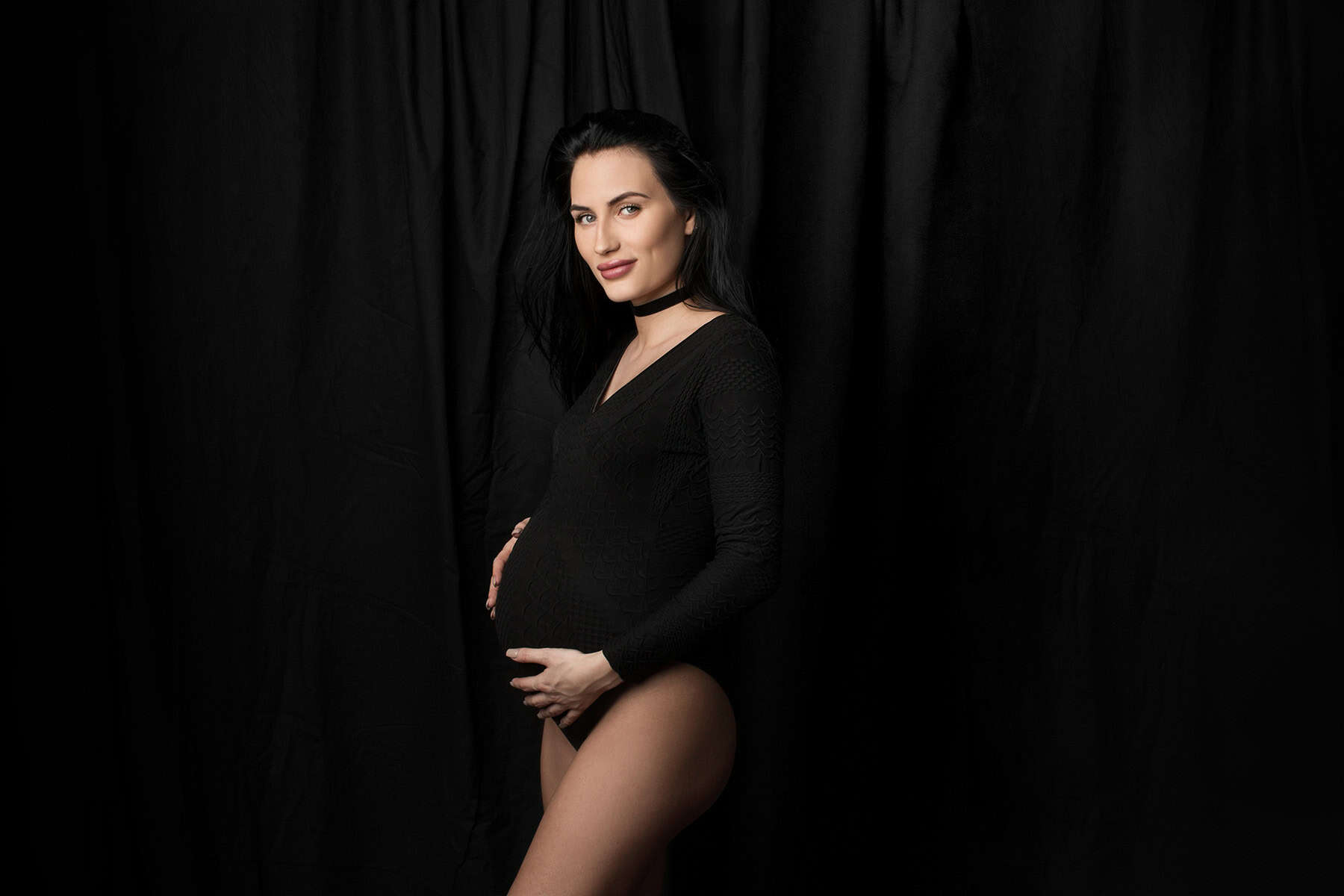 Elegant gravidfotografering av gravid kvinne i svart antrekk, som fremhever skjønnheten og styrken i svangerskapet, mot en mørk bakgrunn for en stilfull gravidfotoseanse.