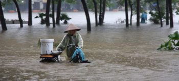 Person wading through floodwaters with equipment in Samoa.