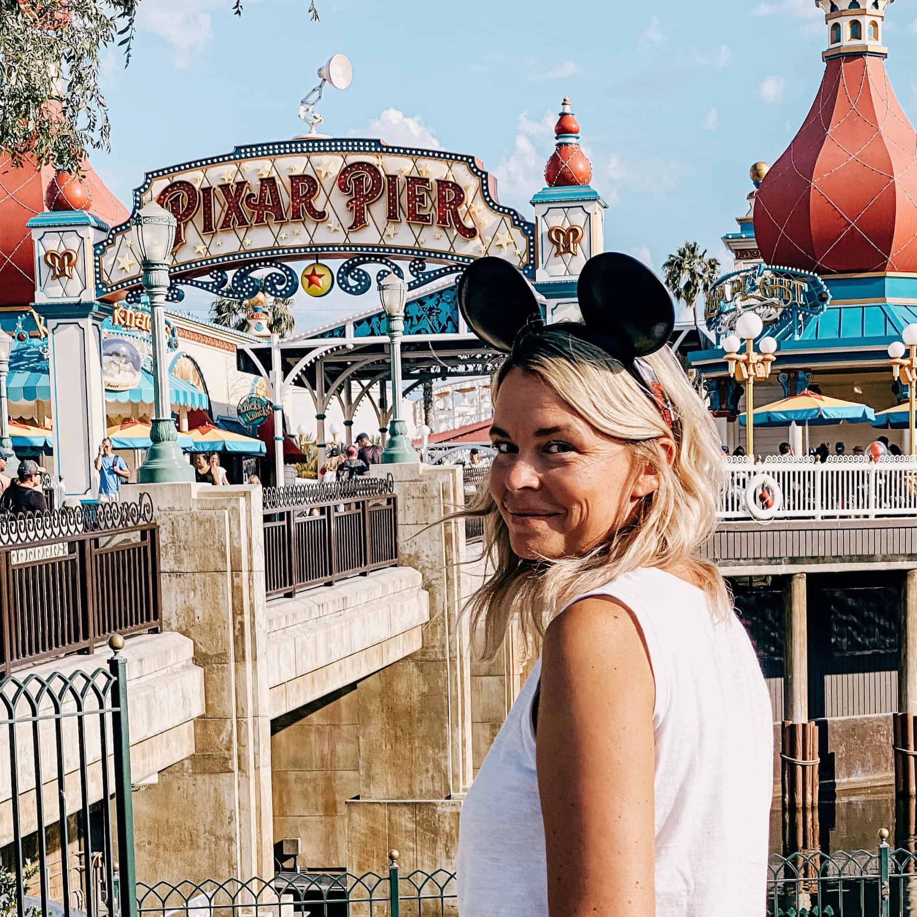 Vibrant woman at Disneyland's Pixar Pier with Mickey Mouse ears, enjoying family vacation fun.