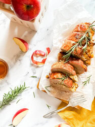 brie stuffed pork tenderloin fillet over parchment paper with apples and a fork over a wooden board