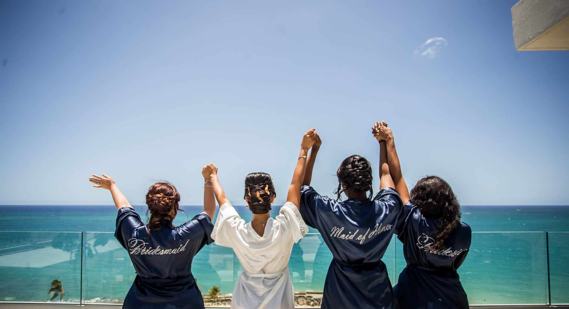 four women holding hands while facing body of water