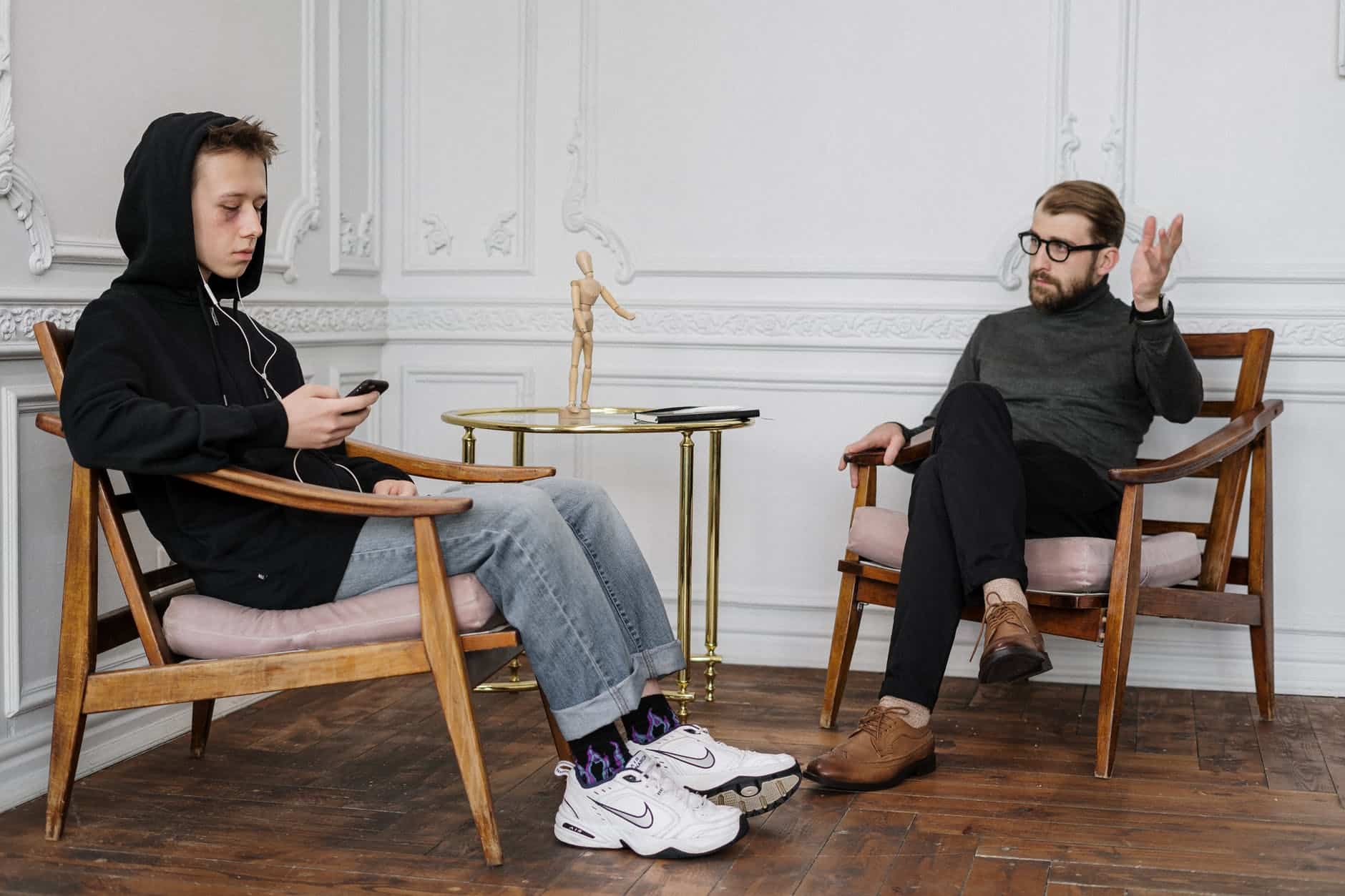 man in black sweater and blue denim jeans sitting on brown wooden rocking chair