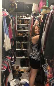 Cluttered walk-in closet with a smiling woman organizing clothes, shoes, and accessories, featuring shelves filled with footwear, clothing rods, and storage boxes, creating an inspiring space for wardrobe organization.