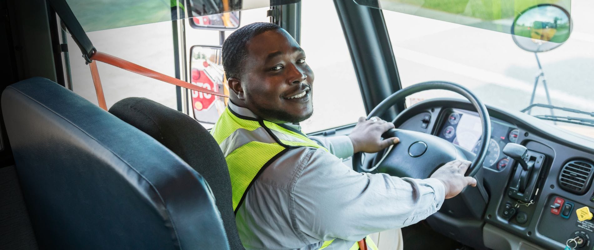 Man smiling in high visibility vest driving bus