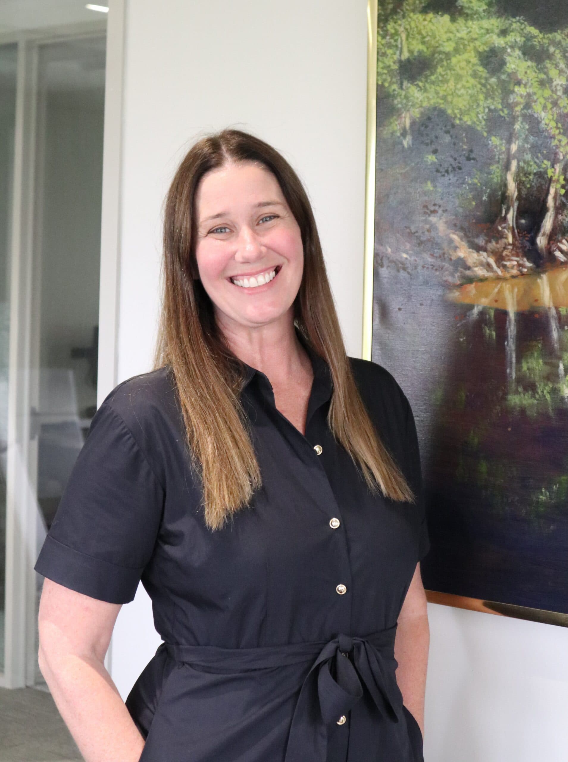 Smiling woman standing beside framed nature painting indoors