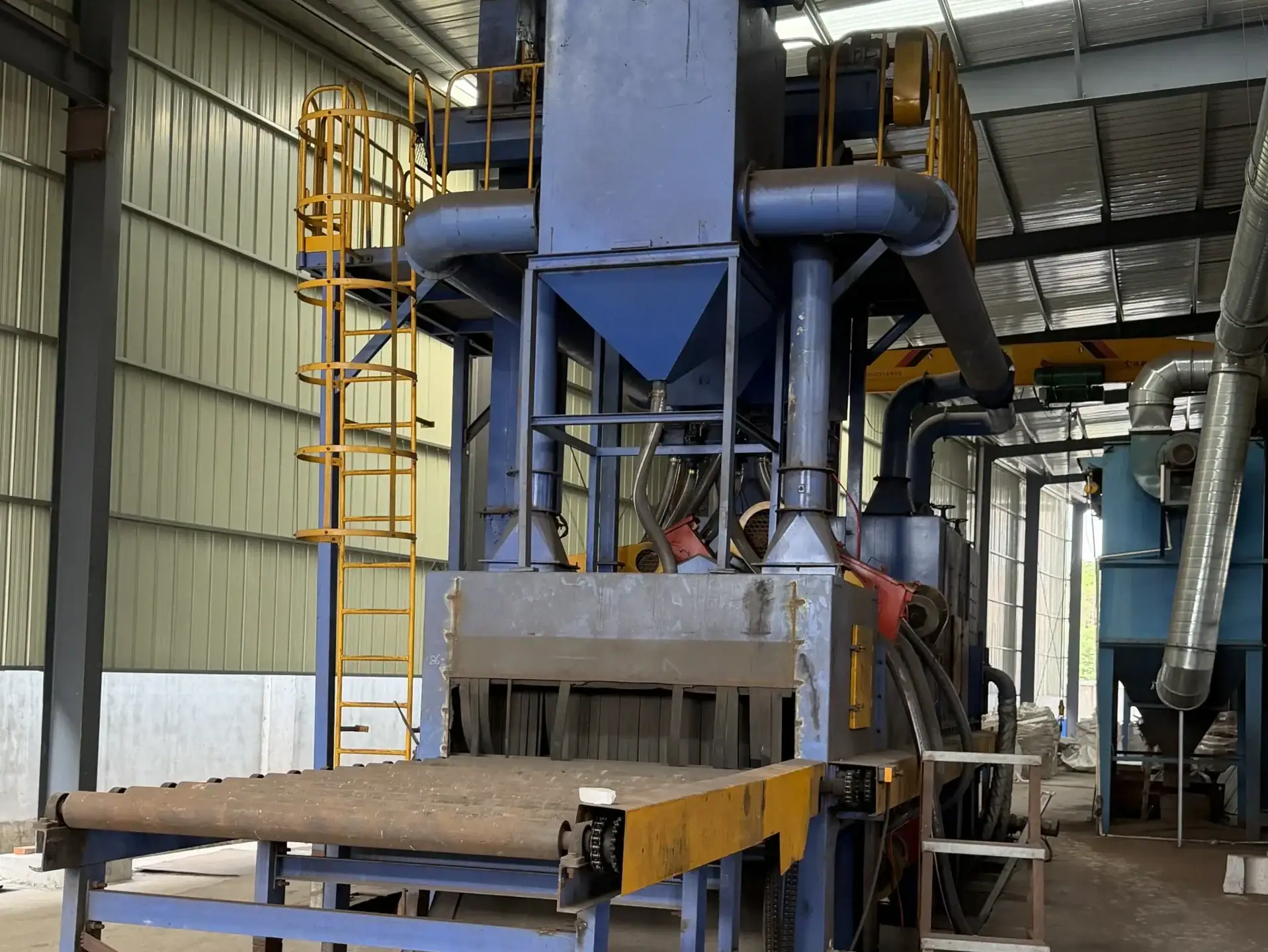 Blue foundry production equipment above a raised work platform with a worker nearby