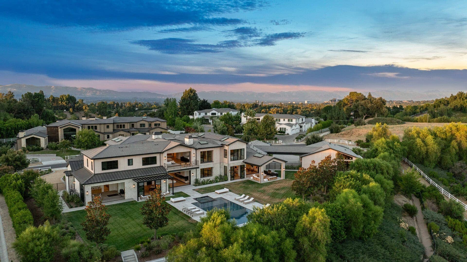 Modern estate with a mix of flat and gently sloped metal roofs, expansive glass windows, and a spacious outdoor pool area.
