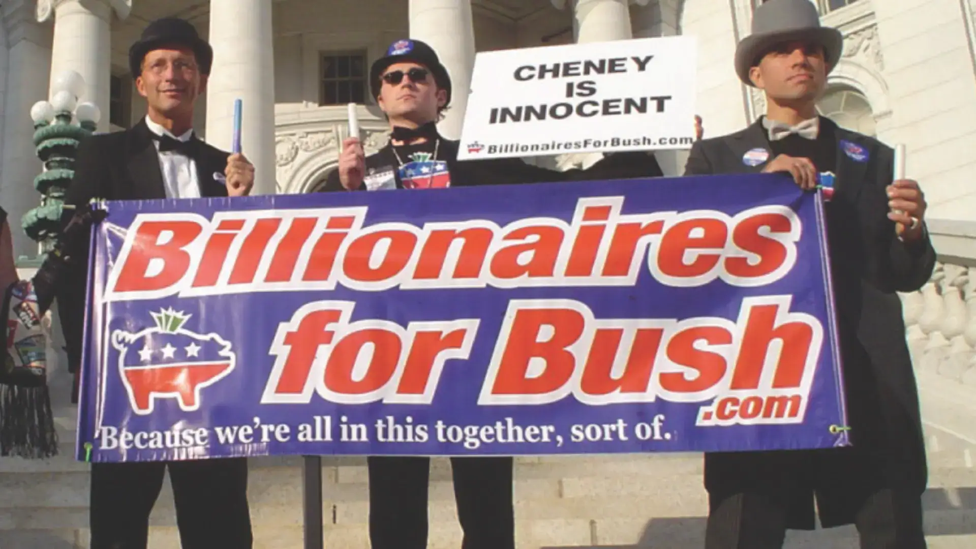 Three men dressed in top hats and tuxedos carry a sign saying "Billionaires for Bush," with another sign stating "Cheney is innocent."