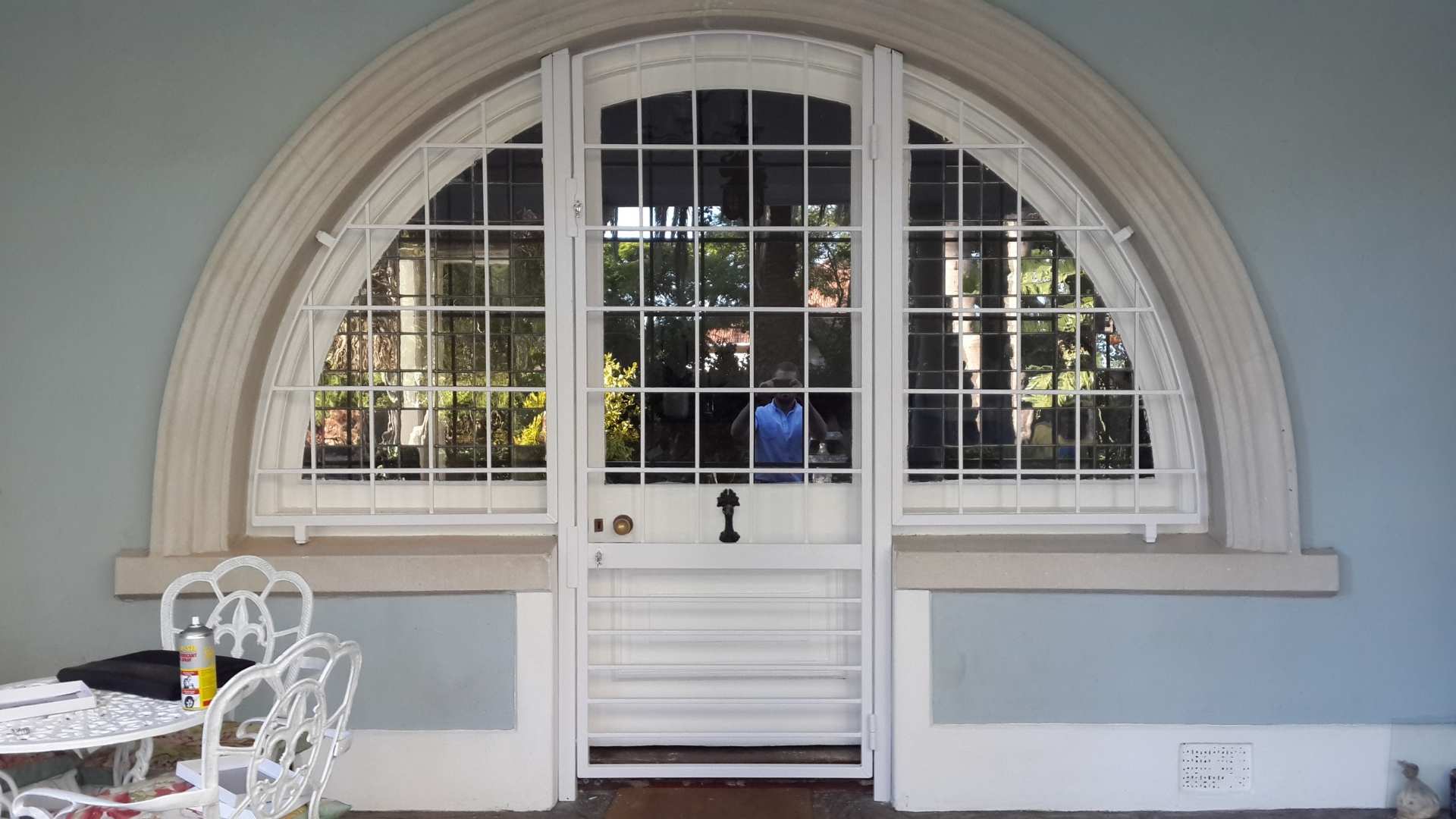 Arched exterior white steel custom gates in a square-grid pattern protecting French doors and flanking windows on a patio.