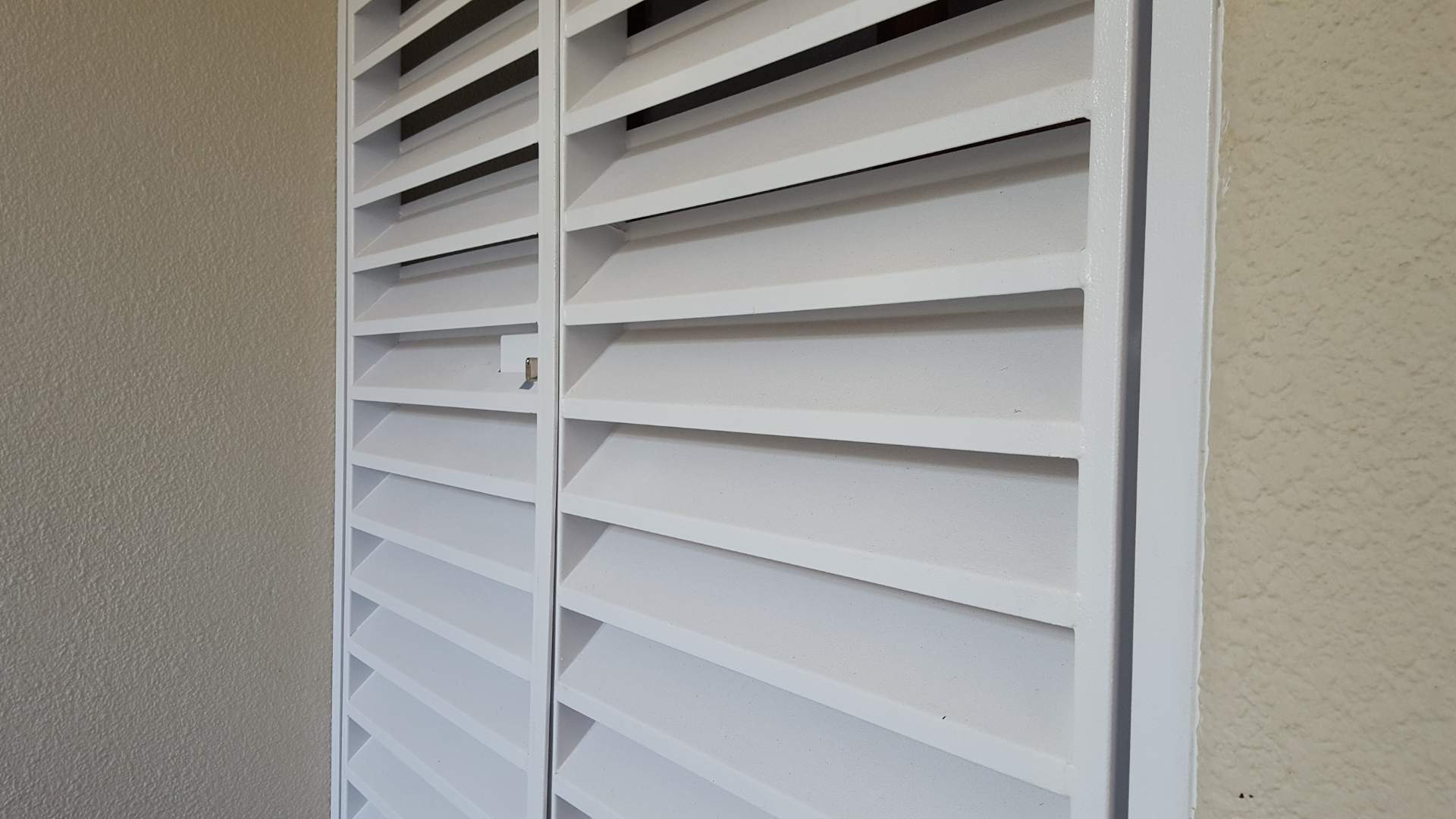 Close-up of modern white louvre security gates door with horizontal slats and central lock, installed in a textured exterior doorway.