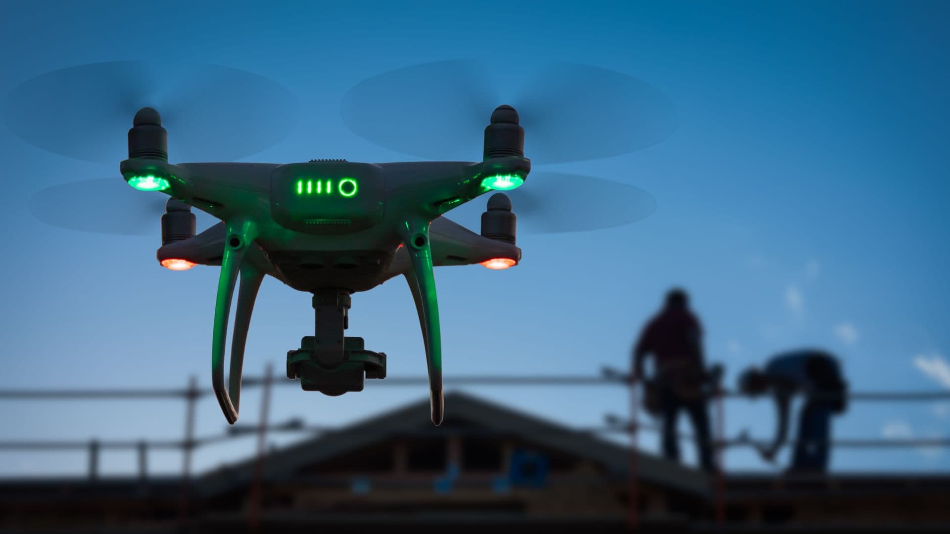 close up of drone with green and red led lights silhouette of people on a roof in background
