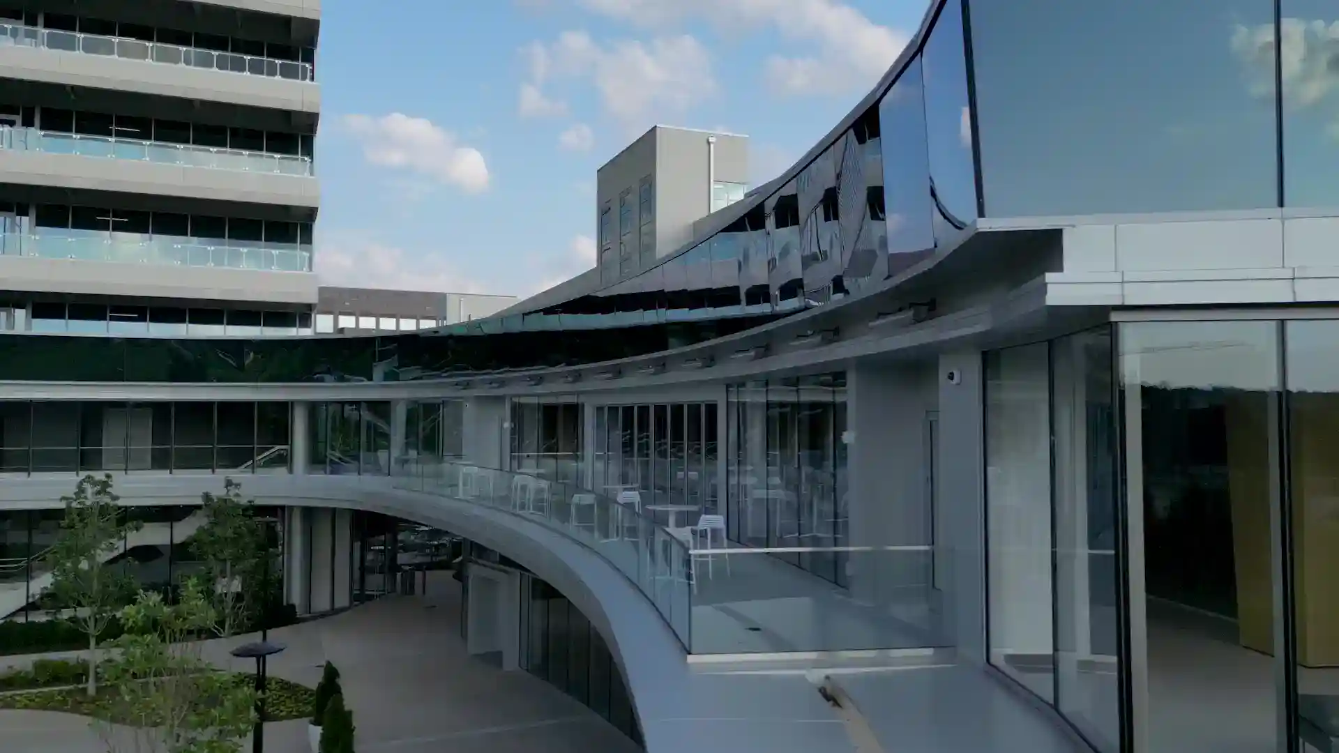 Modern Raleigh mixed-use commercial building featuring curved glass architecture, outdoor terraces, retail storefronts, and landscaped pedestrian spaces in a contemporary urban development.