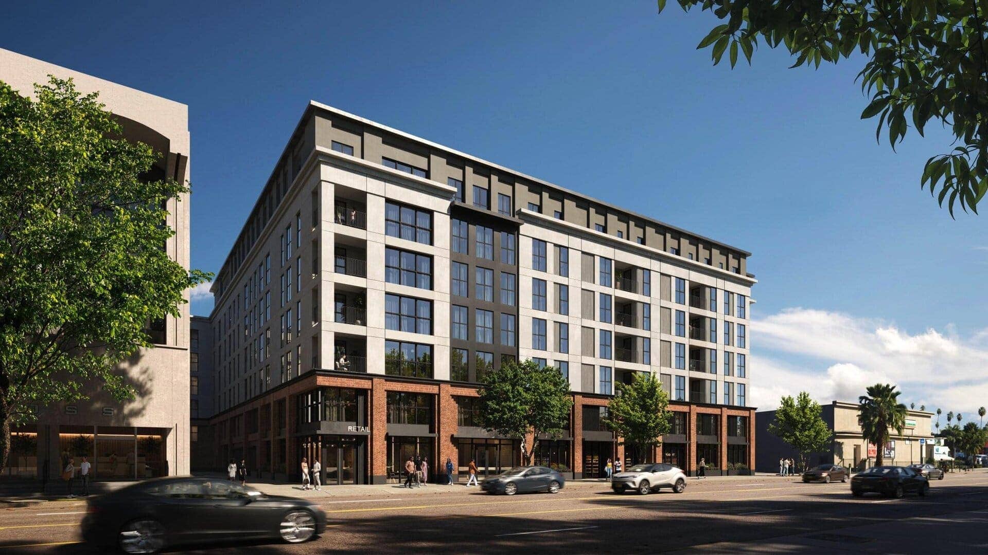 Contemporary mixed-use building with a sleek glass facade, brick accents on the lower floors, and an overhanging roof; set against a blue sky with lush greenery.