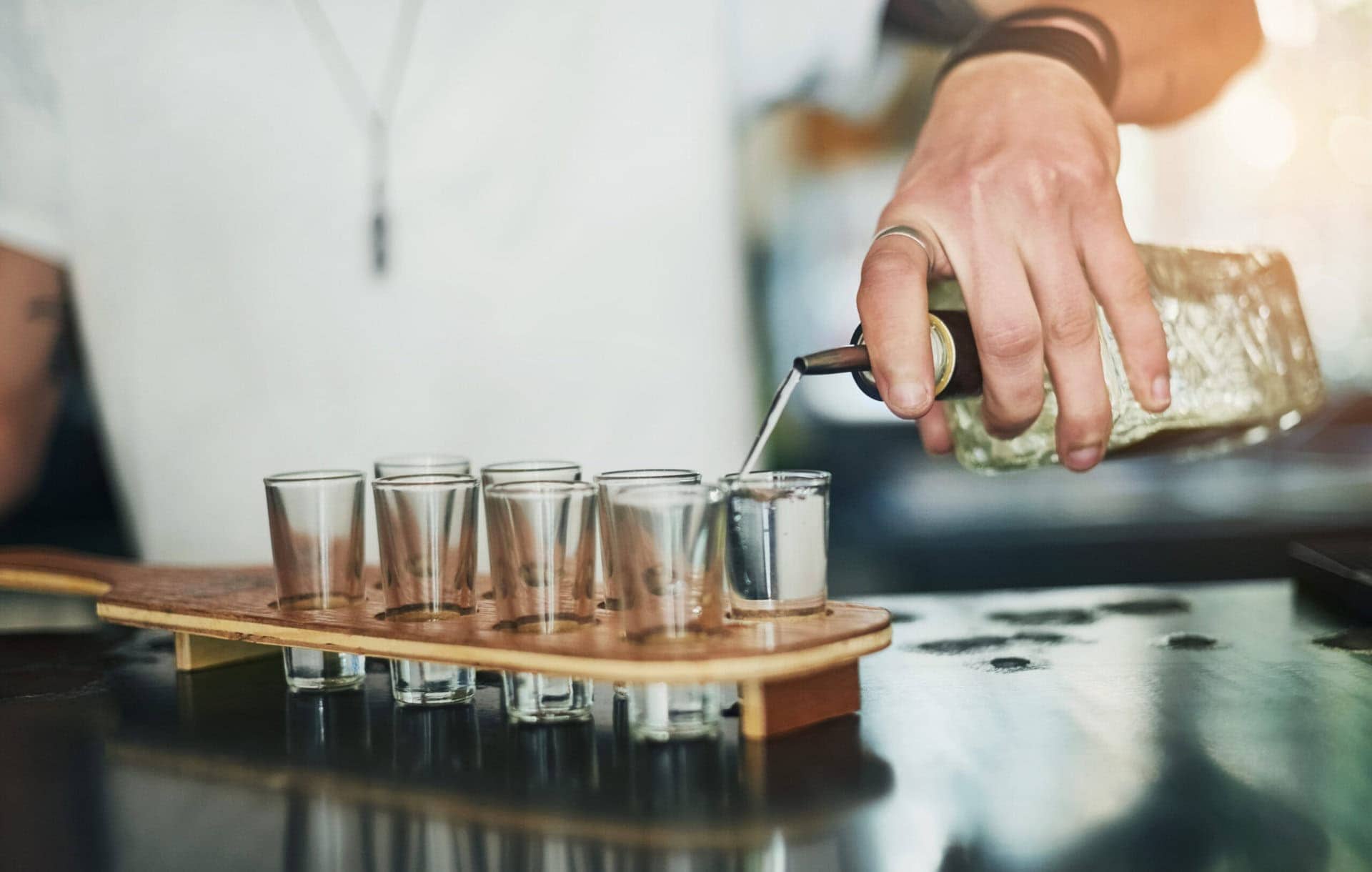 Bartender pouring clear vodka into  flight glasses