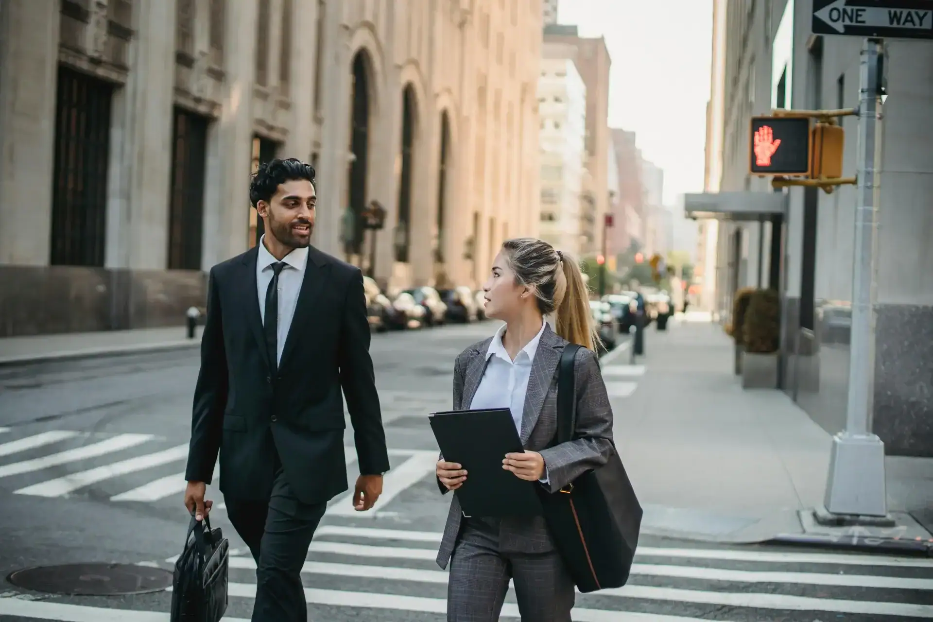 A man and woman in business attire looking at each other while crossing a street