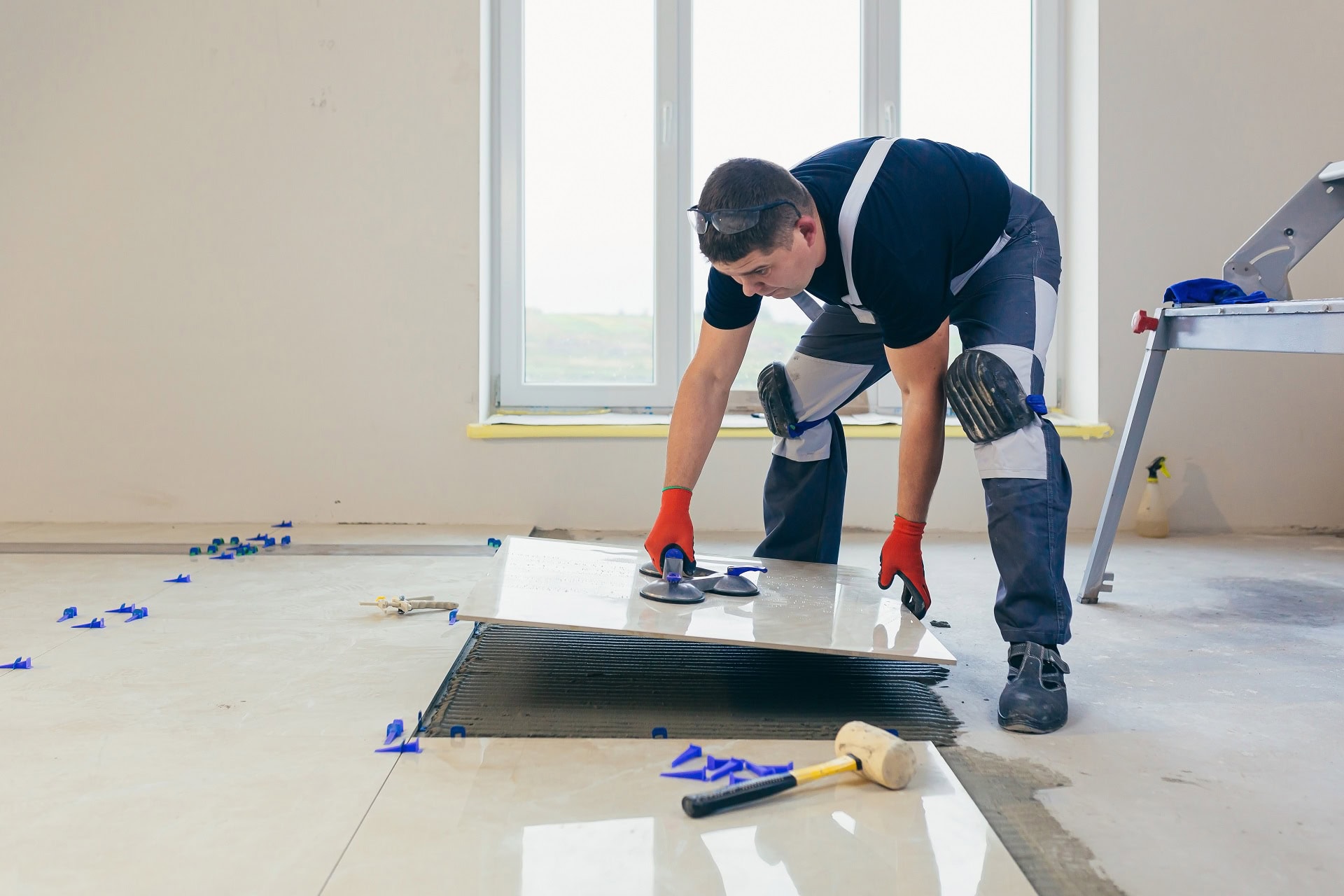 A professional handyman in Coeur D'Alene installing large ceramic floor tiles using a suction cup tool and adhesive in a residential home renovation.