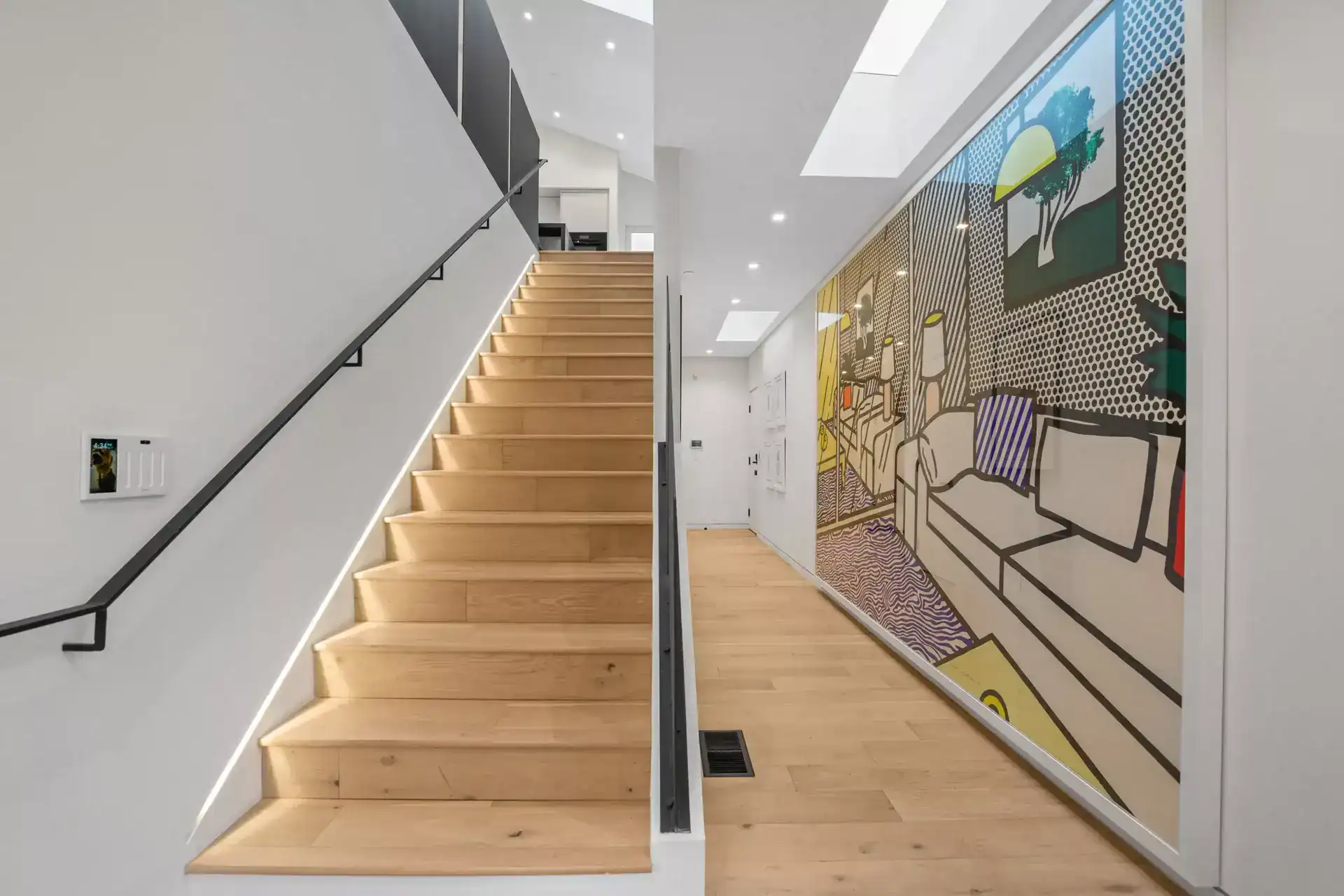 Modern hillside home interior featuring sleek black staircase and colorful contemporary artwork.
