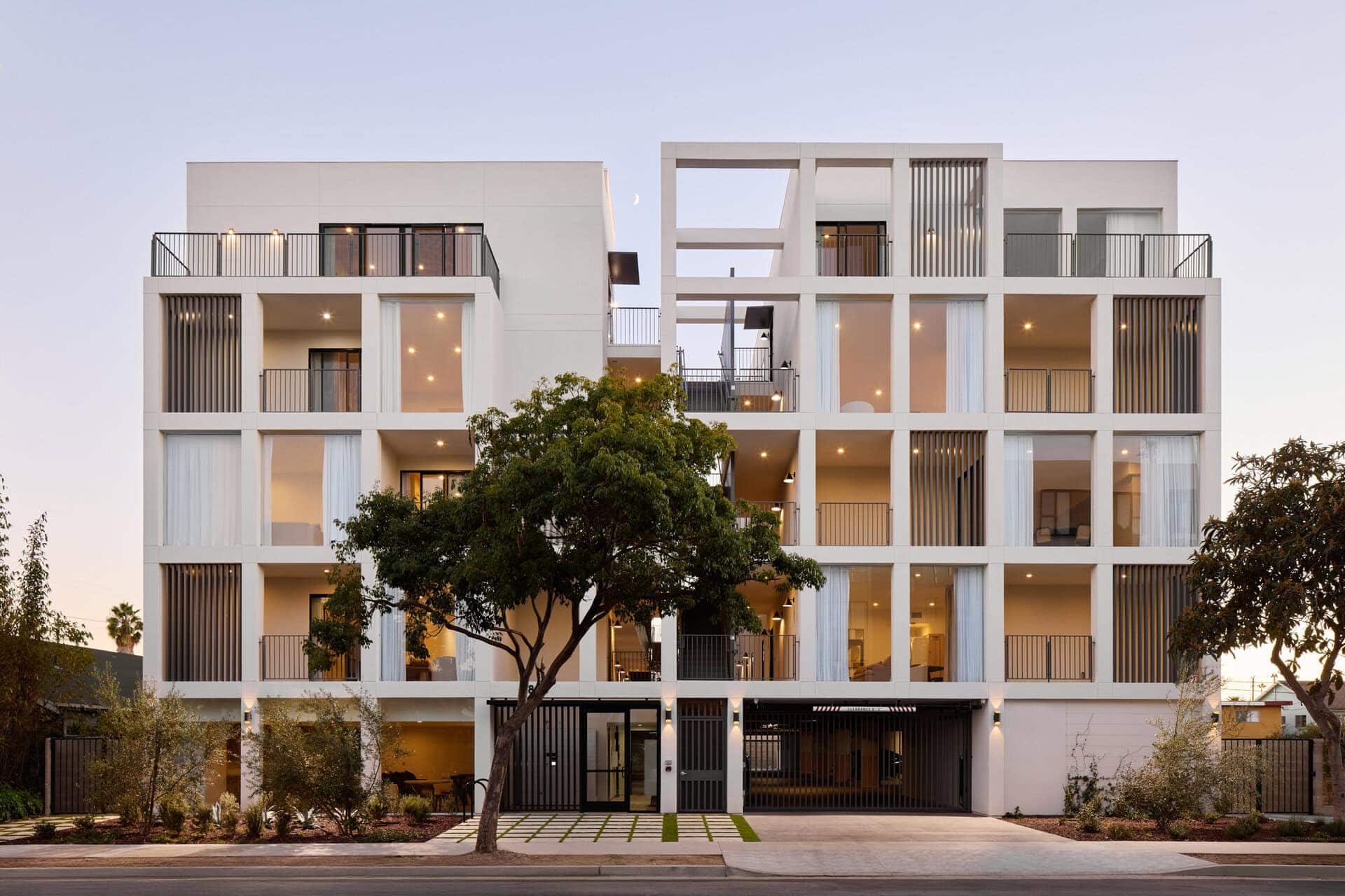 Contemporary white residential building with open balconies, vertical slatted privacy screens, and large glass sliding doors.