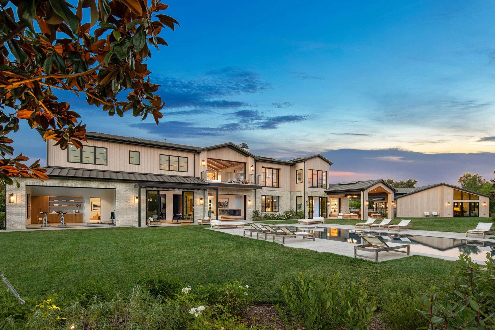 Modern farmhouse-style home with white brick and vertical siding, large black-framed windows, and an outdoor pool area.