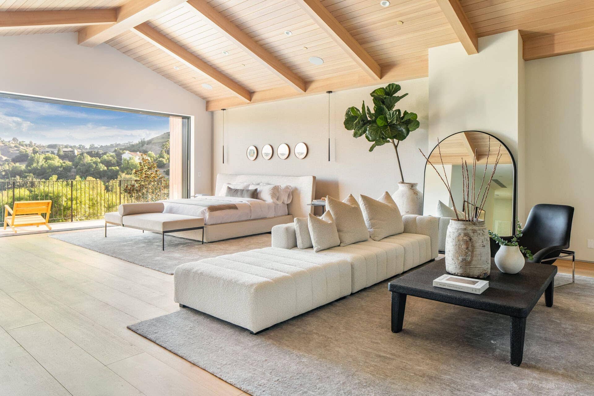 Bright living room with a vaulted wooden ceiling and exposed beams. Large sliding door opens to a scenic outdoor view with natural light. Minimalist decor with neutral tones.