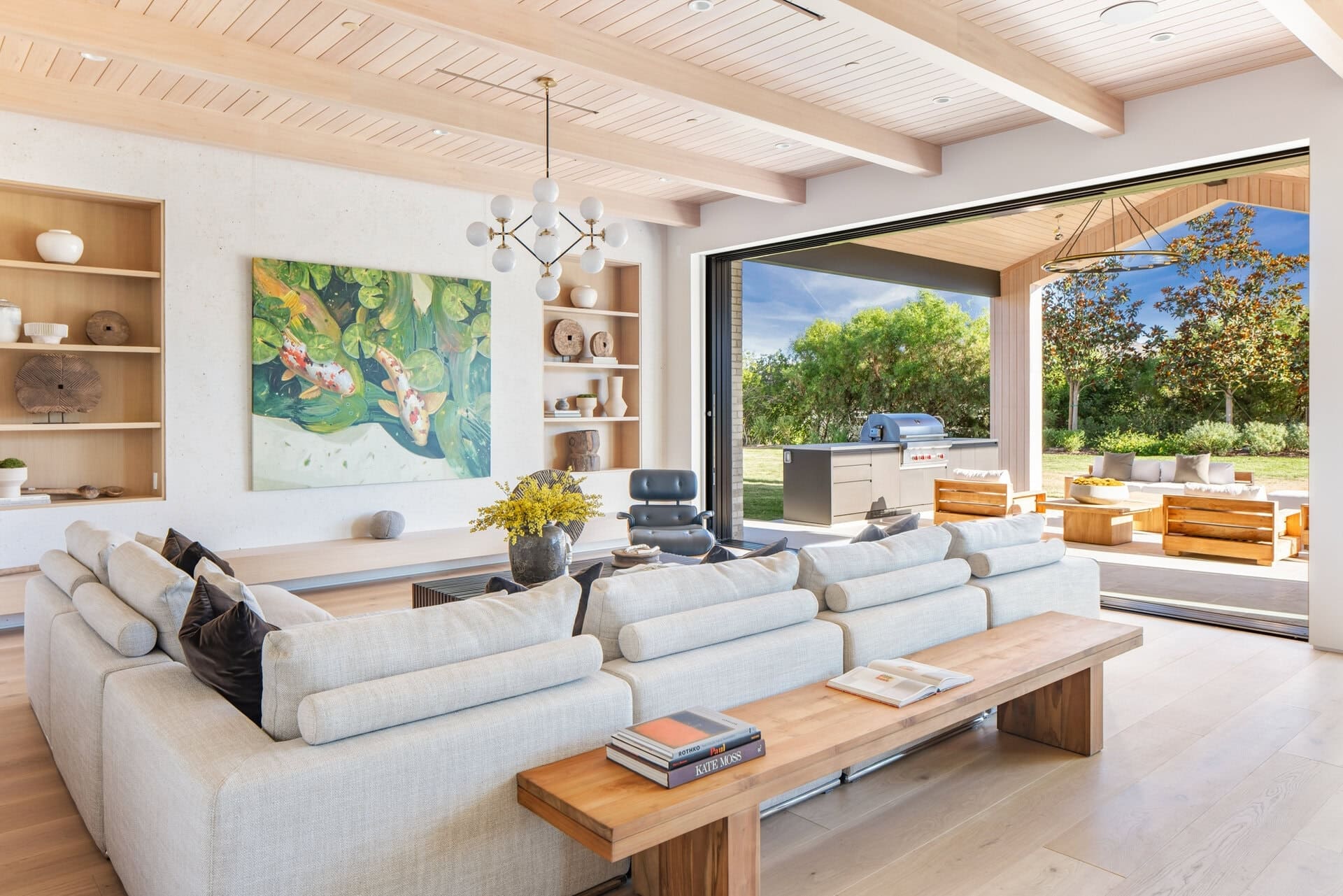 Kitchen with open living space, neutral tones, wood accents, modern chandelier, and large sliding glass doors to outdoor patio, natural light floods the room.