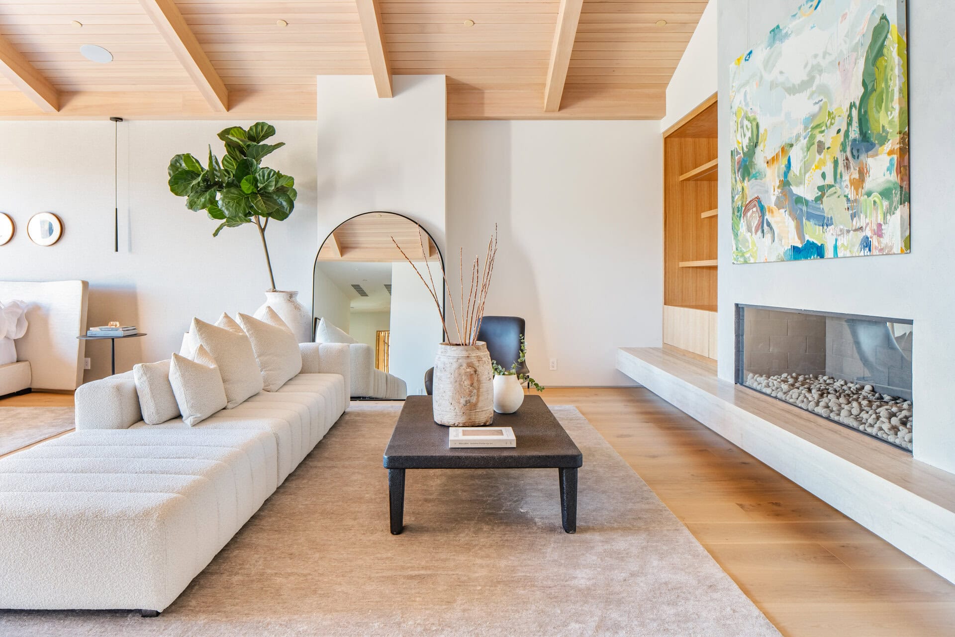 Fuzzy, modern living room with minimalist white sofa, natural wood ceiling beams, and a sleek built-in fireplace.