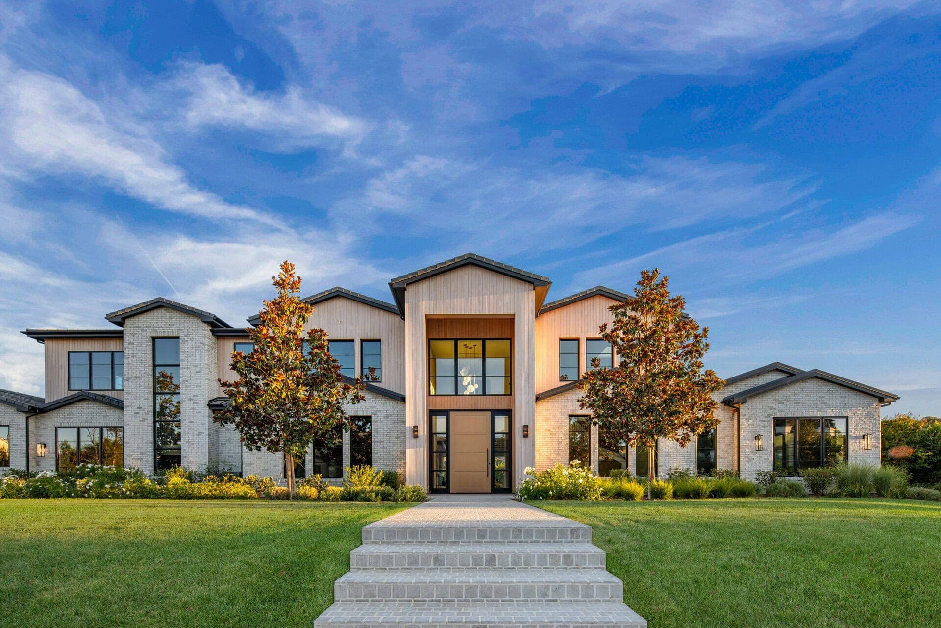 Contemporary two-story house with a mix of light-colored brick and vertical wooden siding, black-framed windows, and a central entrance under a gabled roof.