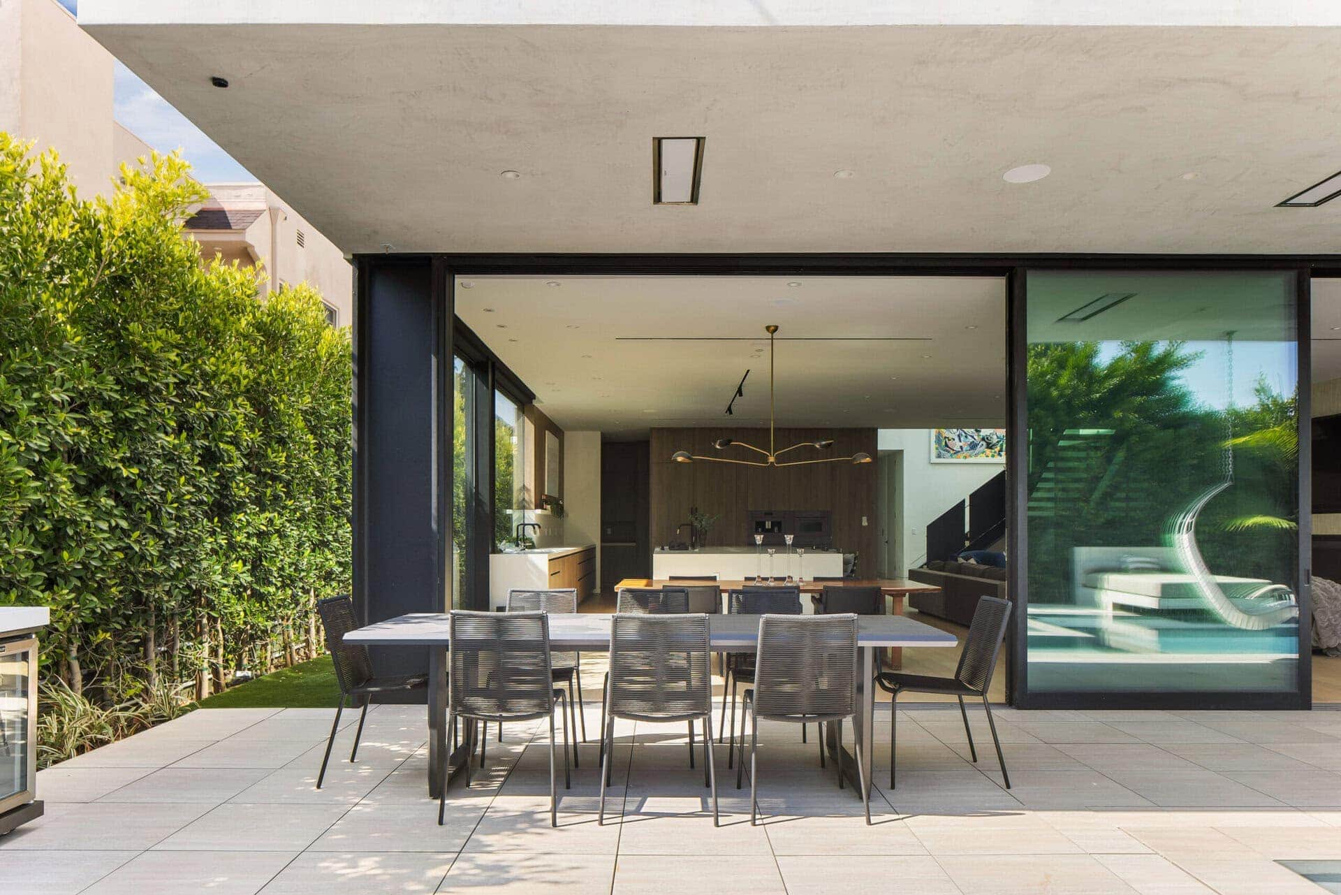 Contemporary modern home with large sliding glass doors, minimalist design, neutral color palette, open-plan indoor-outdoor living, sleek furniture, and integrated lighting.