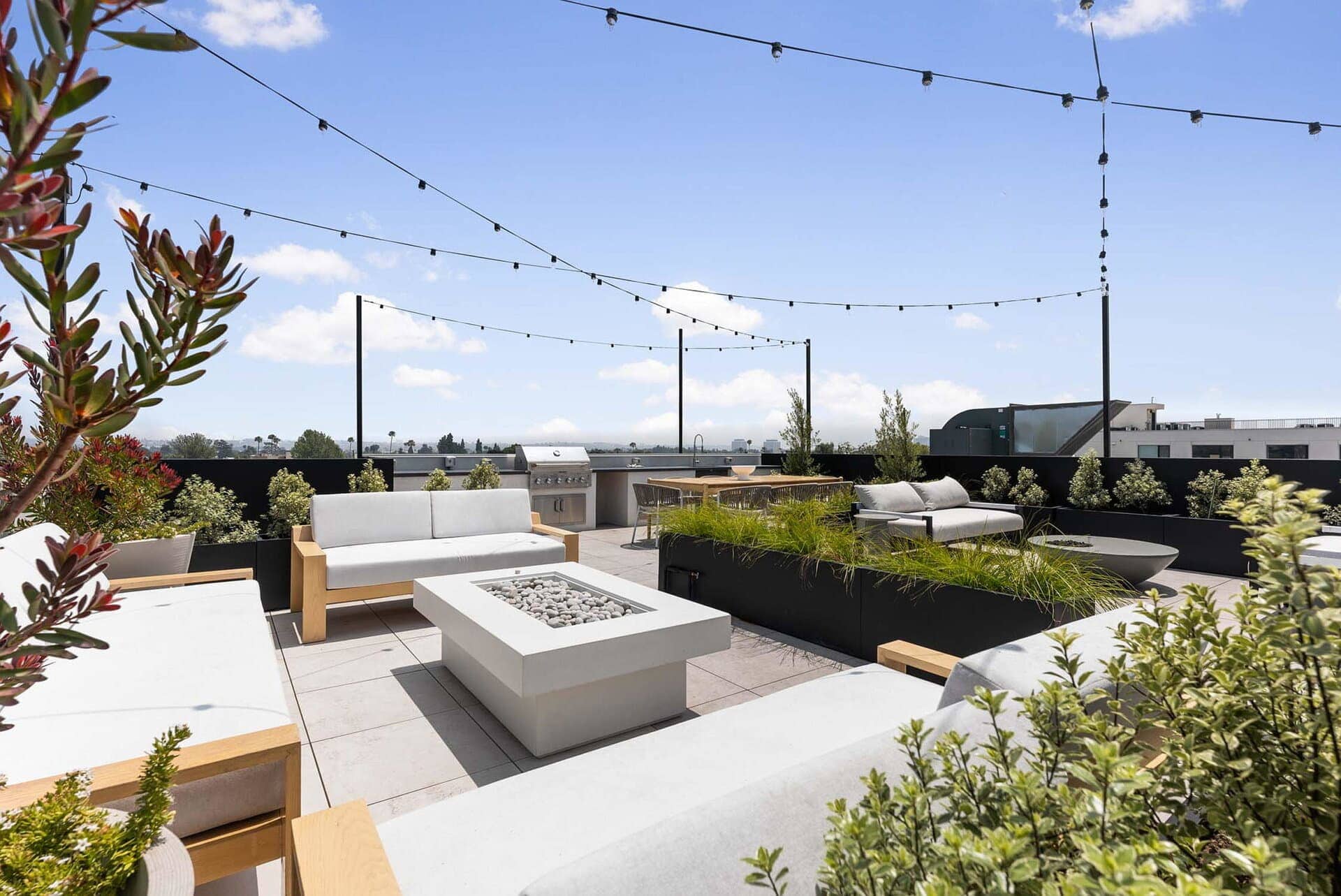 Contemporary rooftop terrace with seating and fire pit, featuring modern outdoor furniture and string lighting.