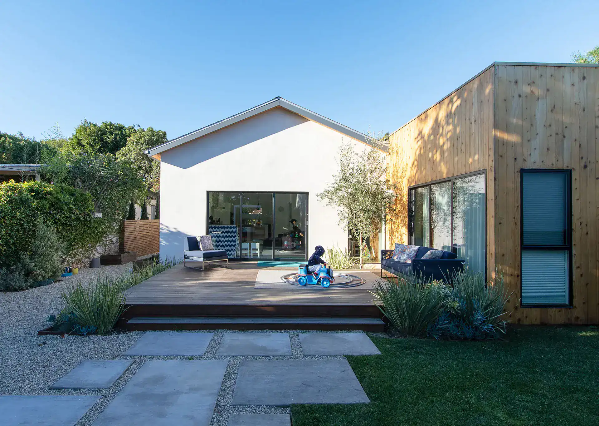 Modern house with a combination of white and wooden exterior walls, large glass sliding doors, and a spacious wooden deck.