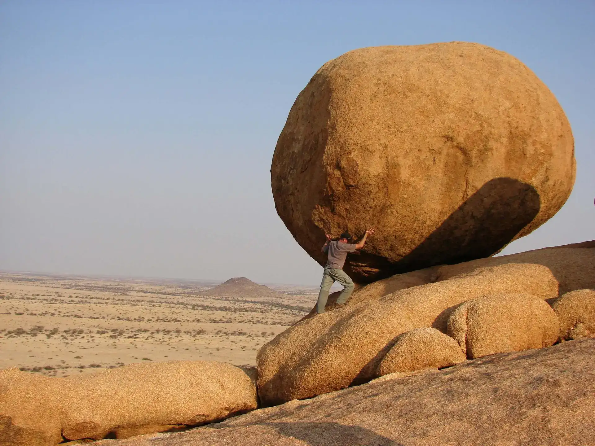 A person pushing a large rock uphill, symbolizing resilience and emotional strength developed through trauma recovery therapy in Farmington Hills, MI.