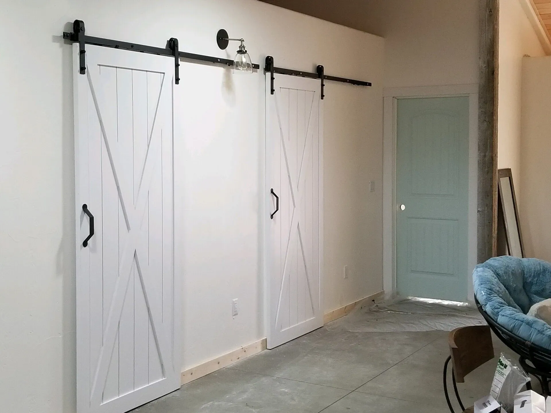 Professional installation of two white wooden sliding barn doors with black hardware in a Coeur D'Alene home, showcasing custom carpentry services.