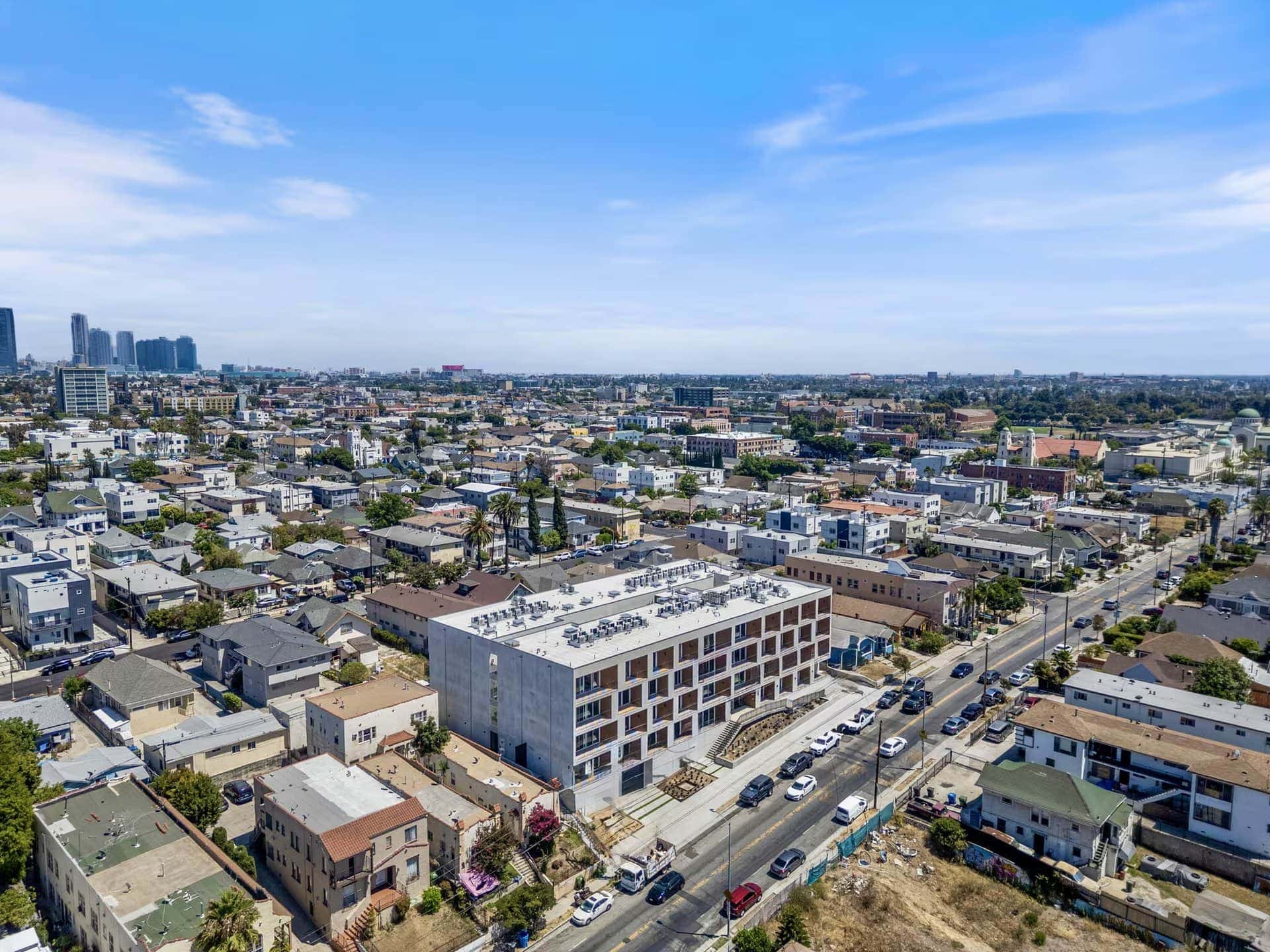 Modern multi-story apartment building with a concrete facade and rows of balconies, set amidst a dense residential neighborhood.