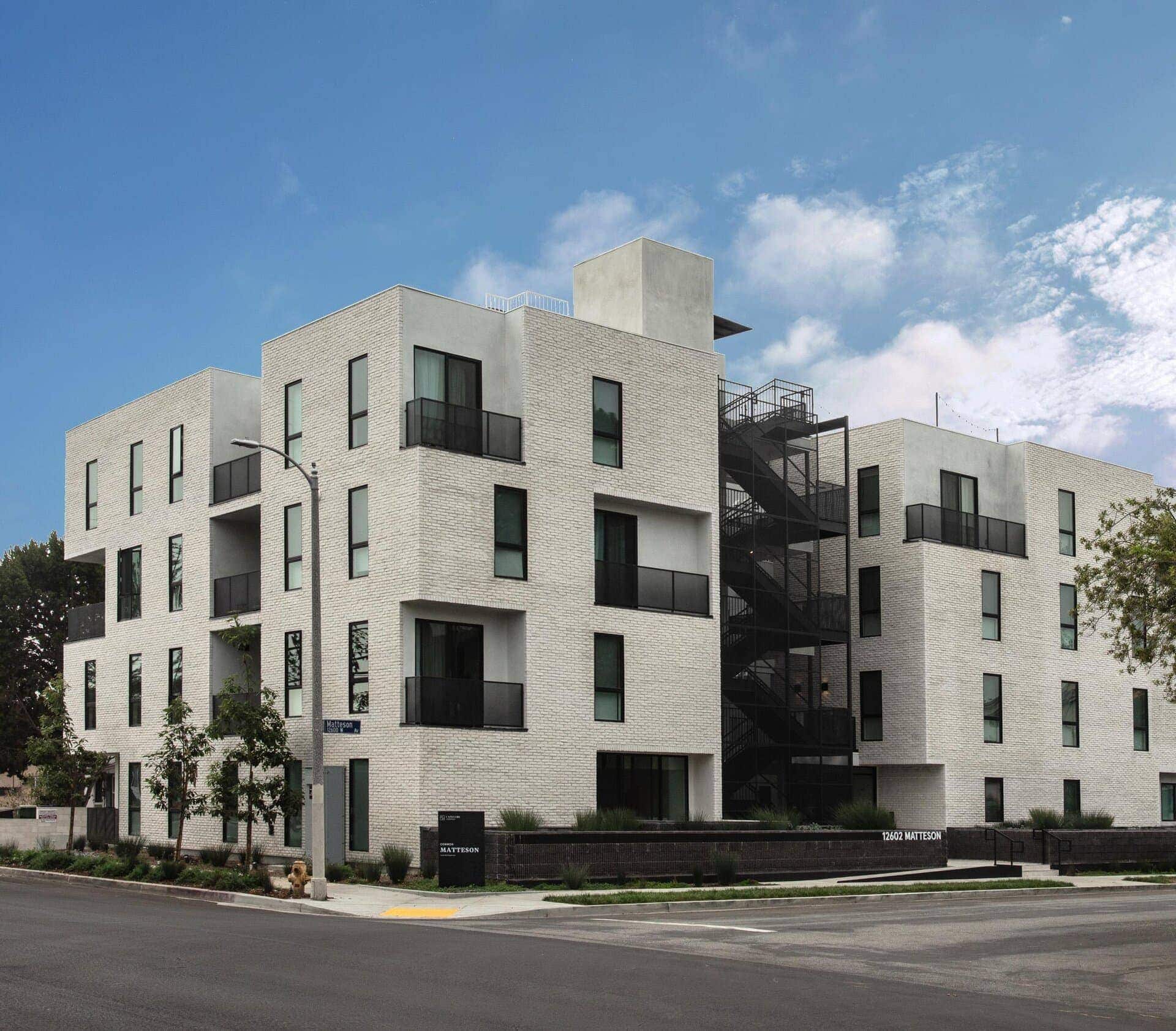 Contemporary residential apartment building with white brick facade and black balcony railings.