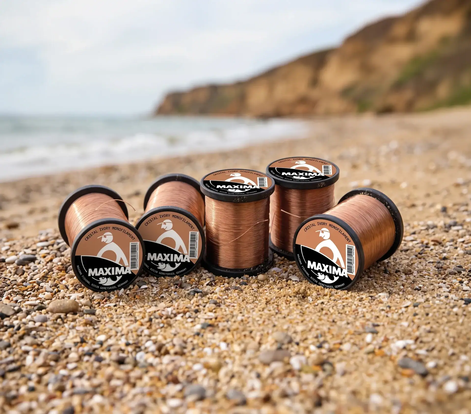 Several Maxima bronze Cristal Ivory monofilament fishing line spools on a sandy beach by the sea