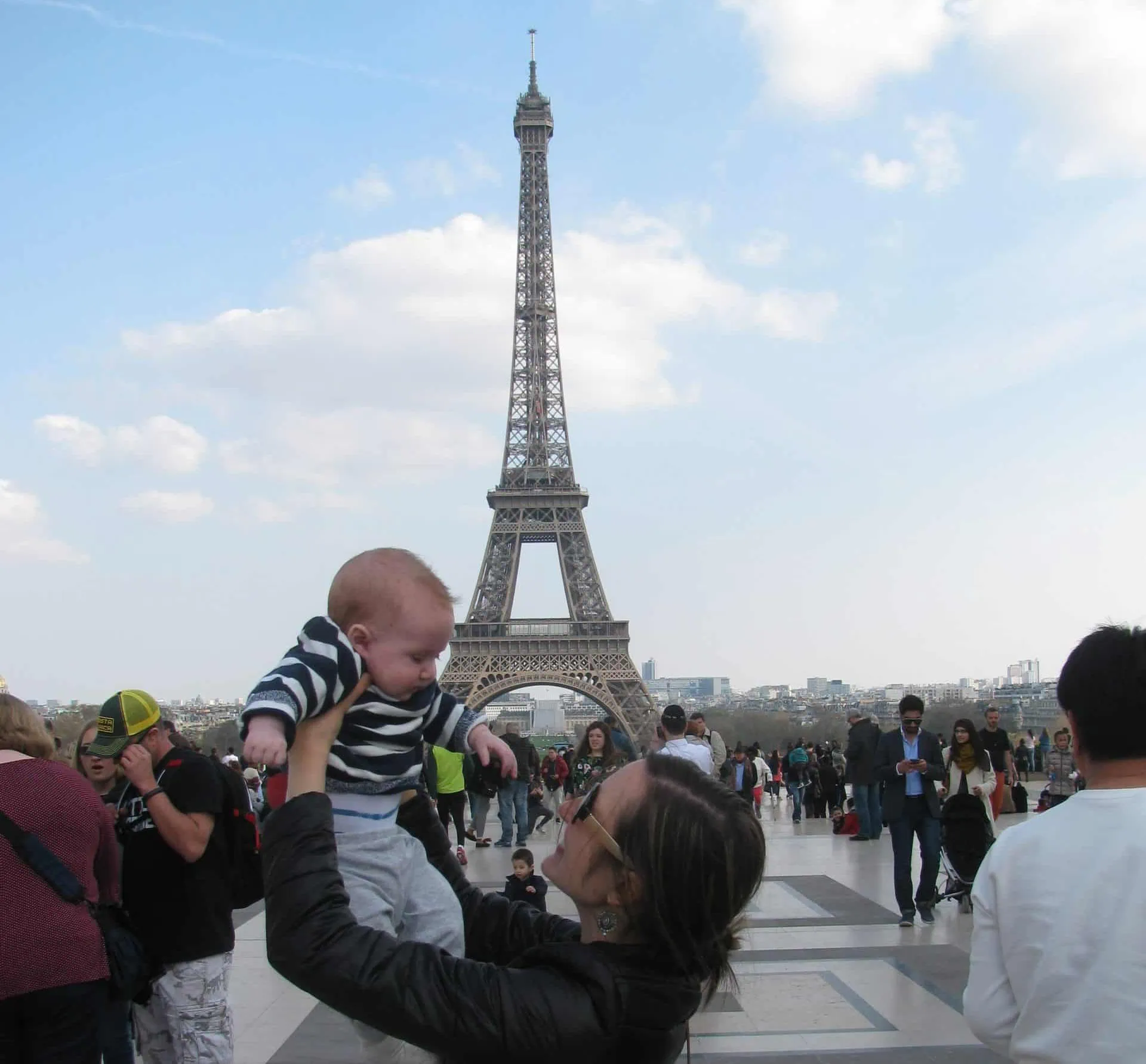 Mom lifting a baby in front of the Eiffel tower.