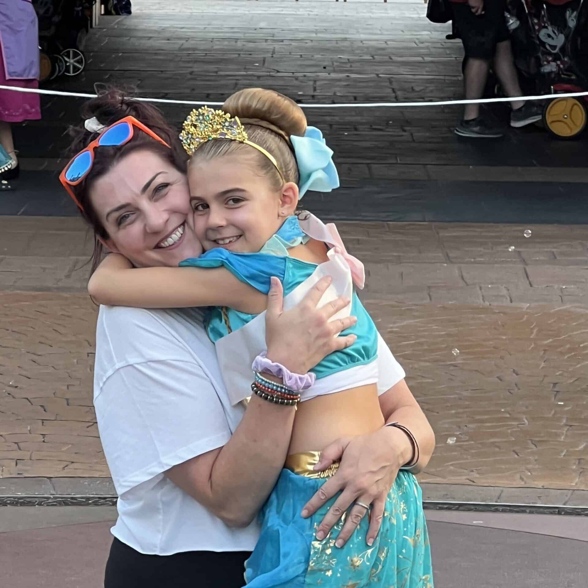 Smiling woman and girl hugging at Disneyland, wearing princess costumes and accessories.