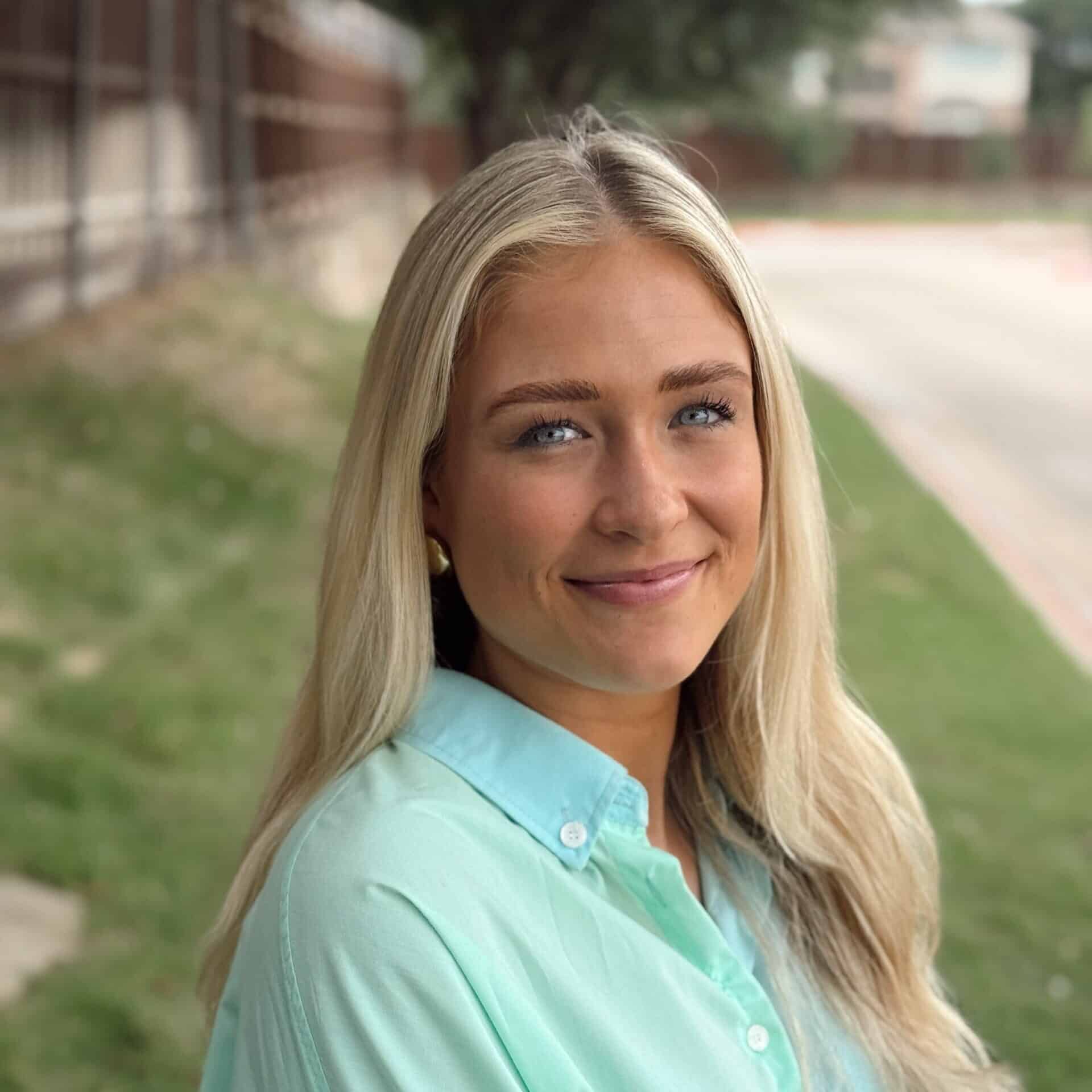 Blonde woman smiling outdoors in a light green shirt, enjoying vacation or nature escape.