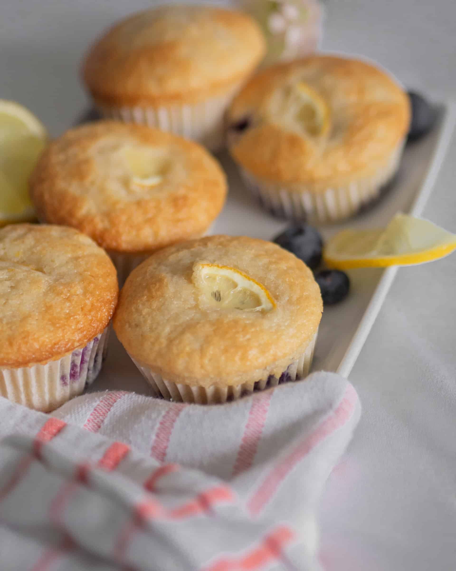 lemon blueberry muffin on a tray with more lemons and blueberries around , from the side