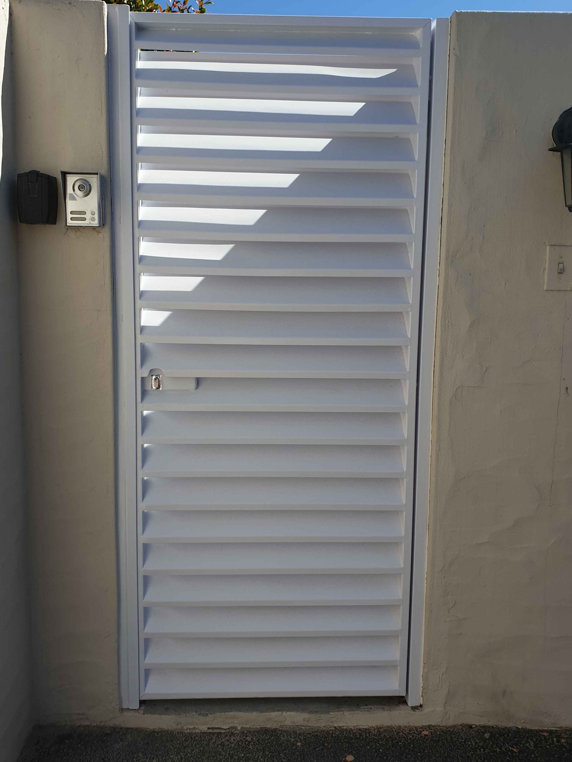 White Louvre security gates door installed at a narrow passage entrance, providing ventilation and security.